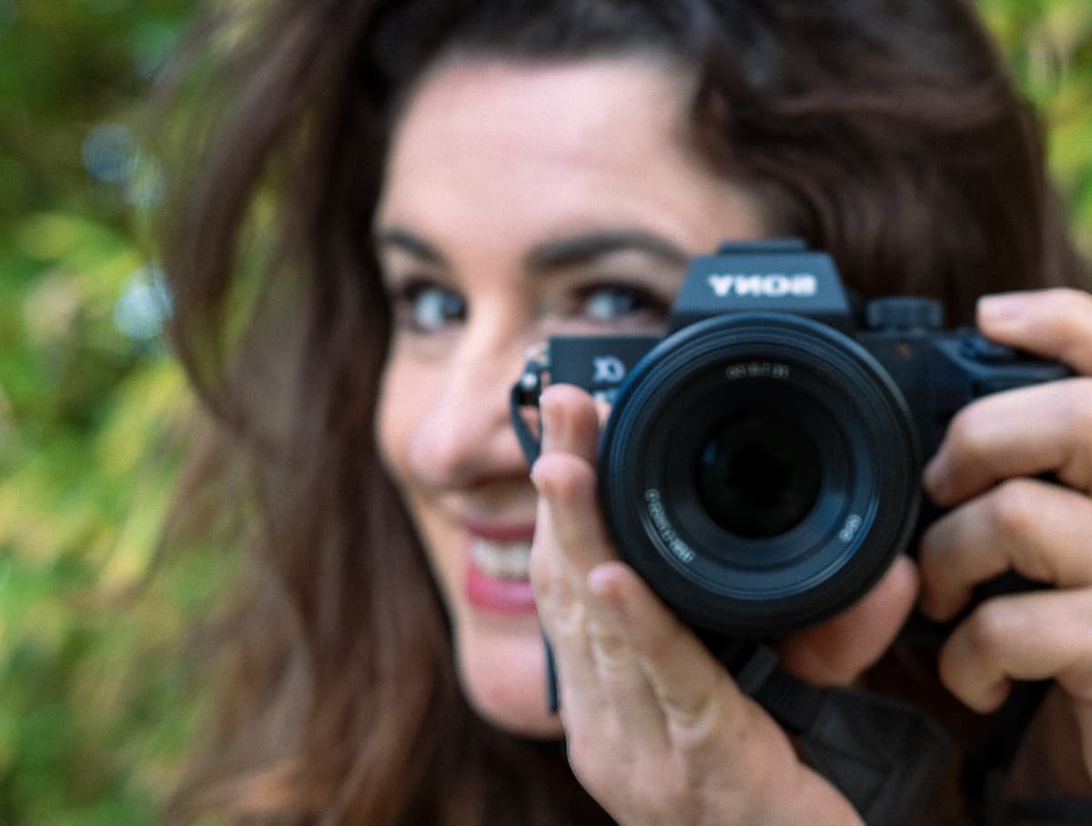 photo d'un visage en arrière plan qui sourit et qui tient un appareil photo au premier plan