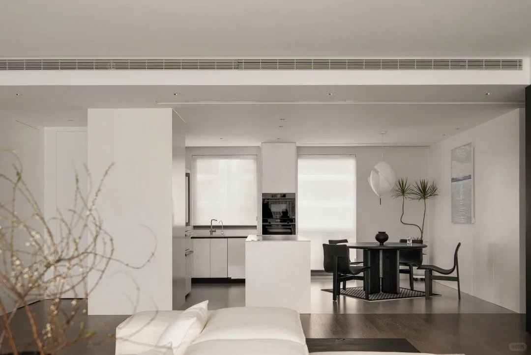 Open-concept kitchen and dining area with white walls, black dining table, black chairs, and modern decor.