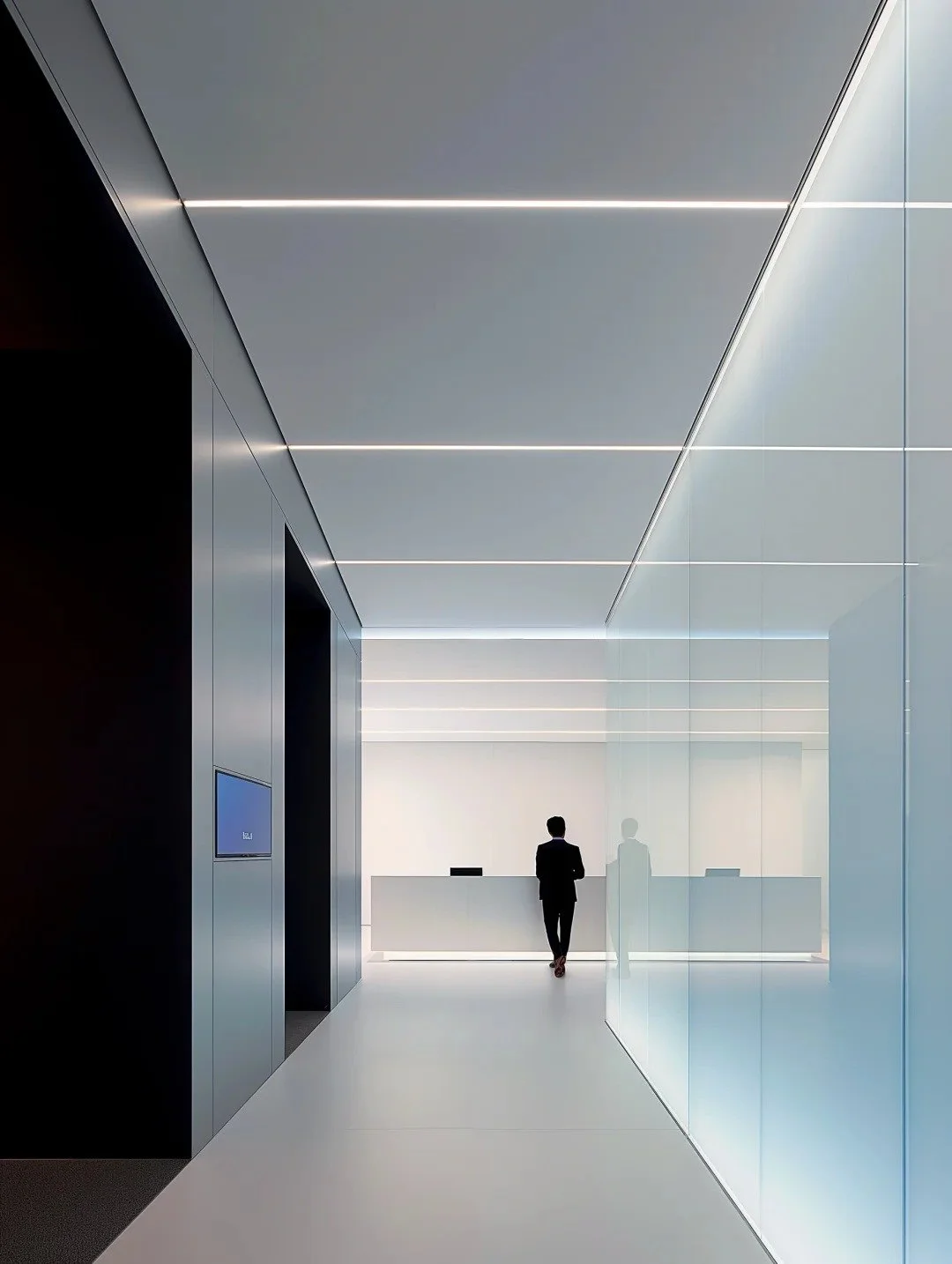 Modern office lobby with sleek white and gray design, featuring a reception desk and a person walking towards it.