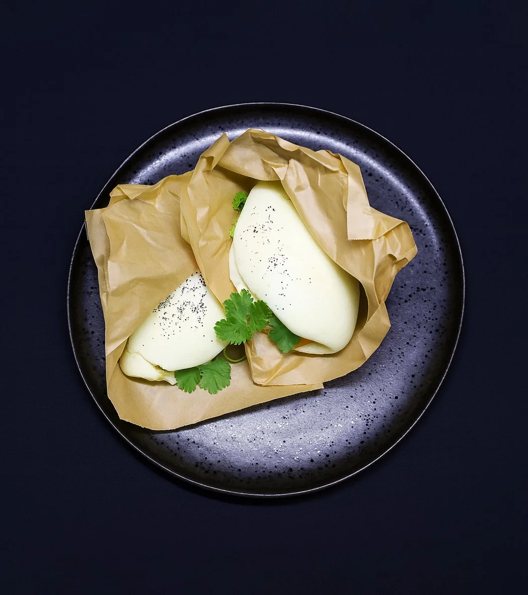 Zwei pochierte Eier auf braunem Backpapier, garniert mit Koriander und Pfeffer, auf einer schwarzen Platte