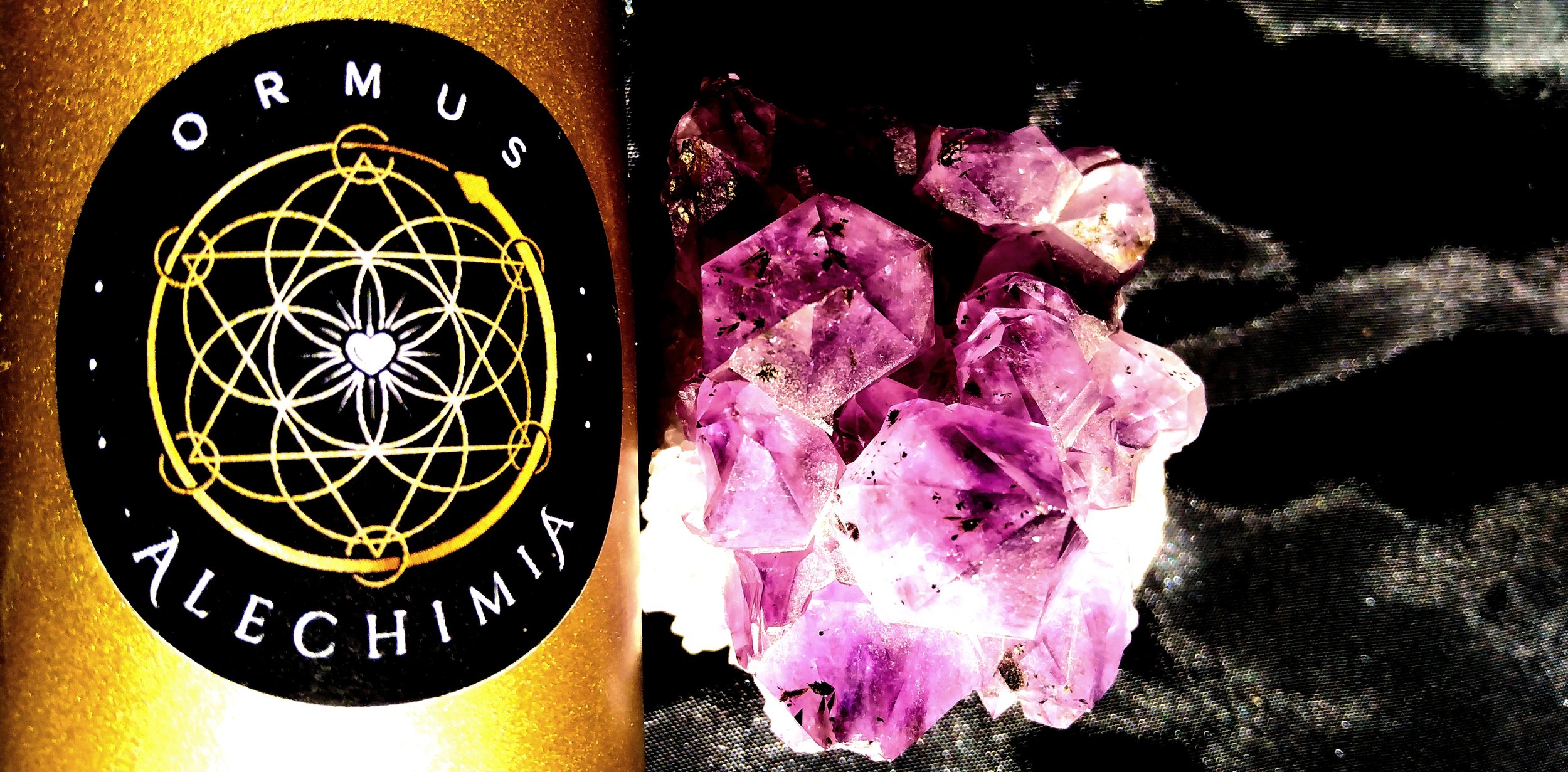 A black and white patch with sacred geometric designs and the words 'Ormus Alechimia' on the left side; next to it, amethyst crystals on a dark surface.