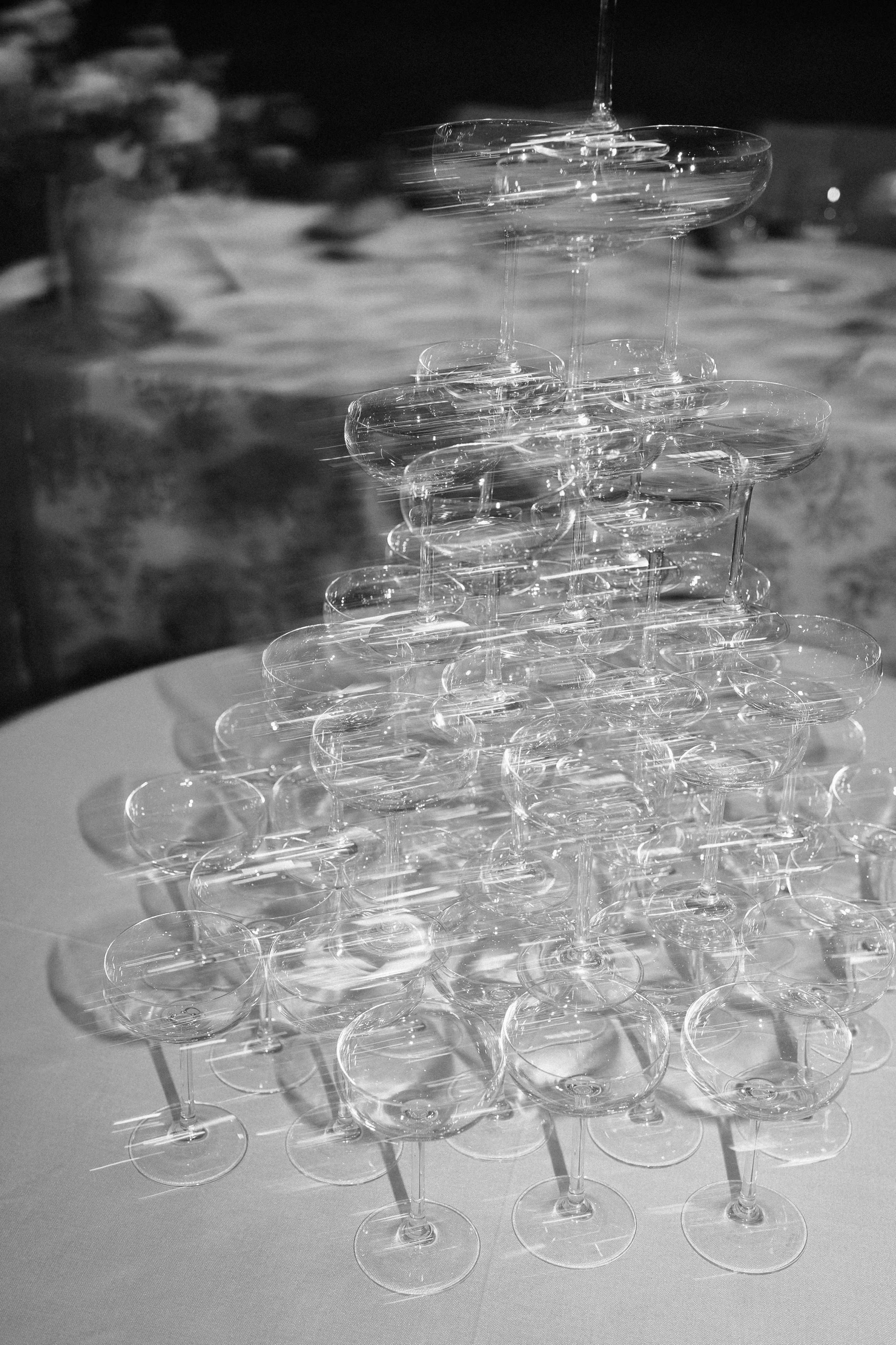 A pyramid of clear champagne glasses arranged on a white tablecloth, with a blurred background on a luxury wedding in Spain.