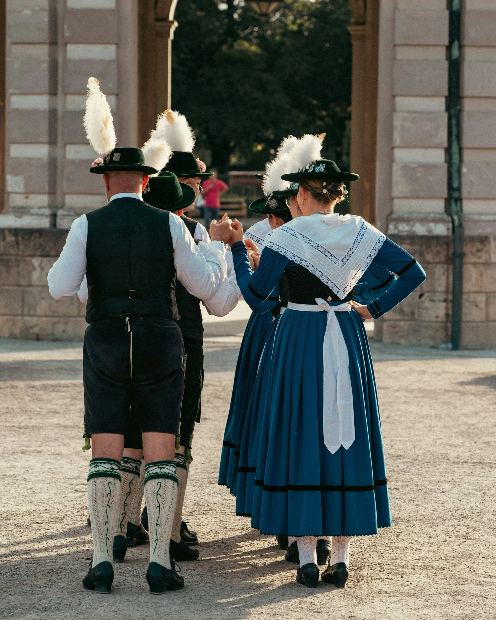 Group of people dressed in traditional Bavarian clothing, standing together and interacting outdoors.