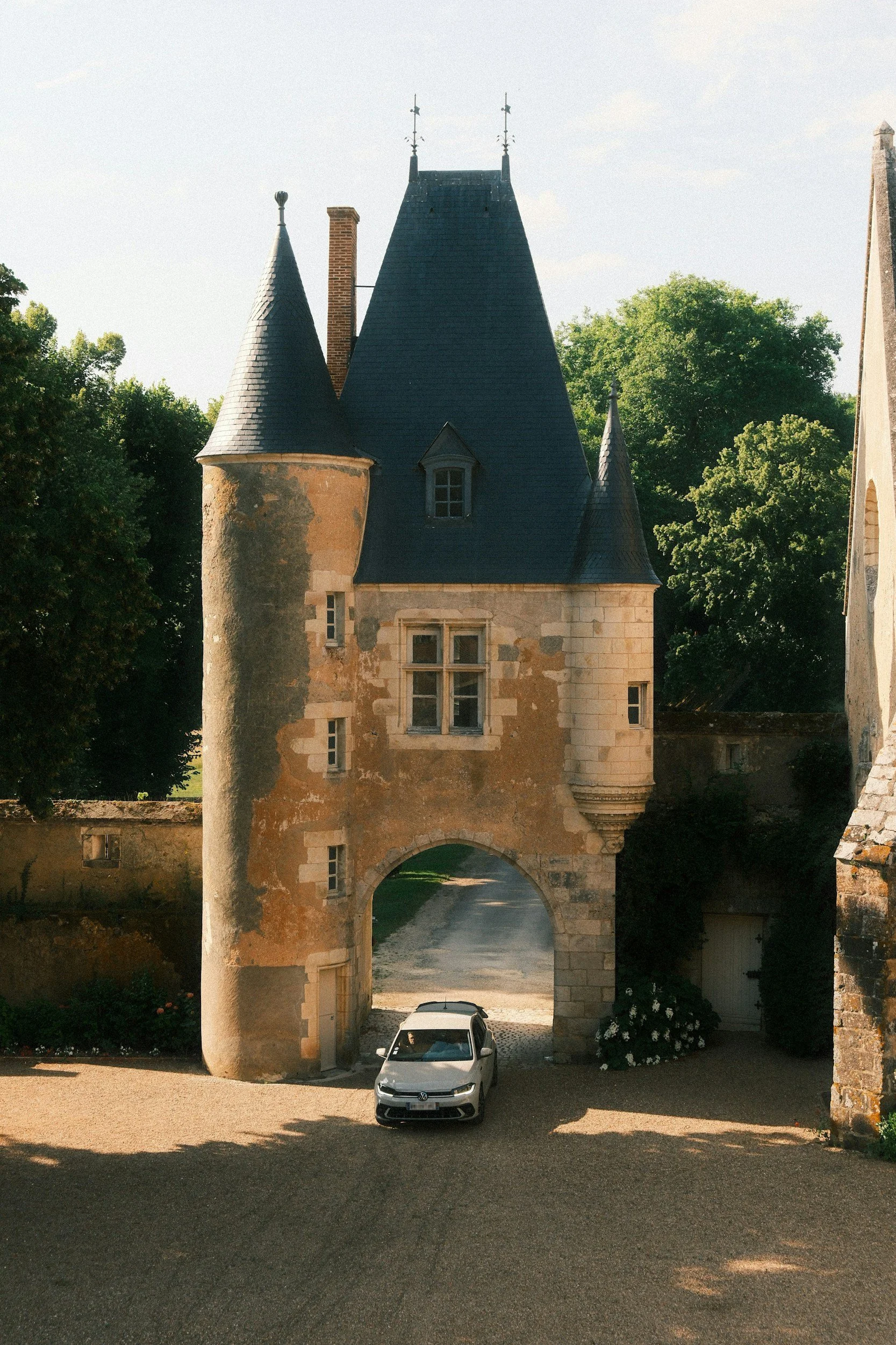 A castle-like building with a tower, arched driveway, and a silver Volkswagen car parked underneath.