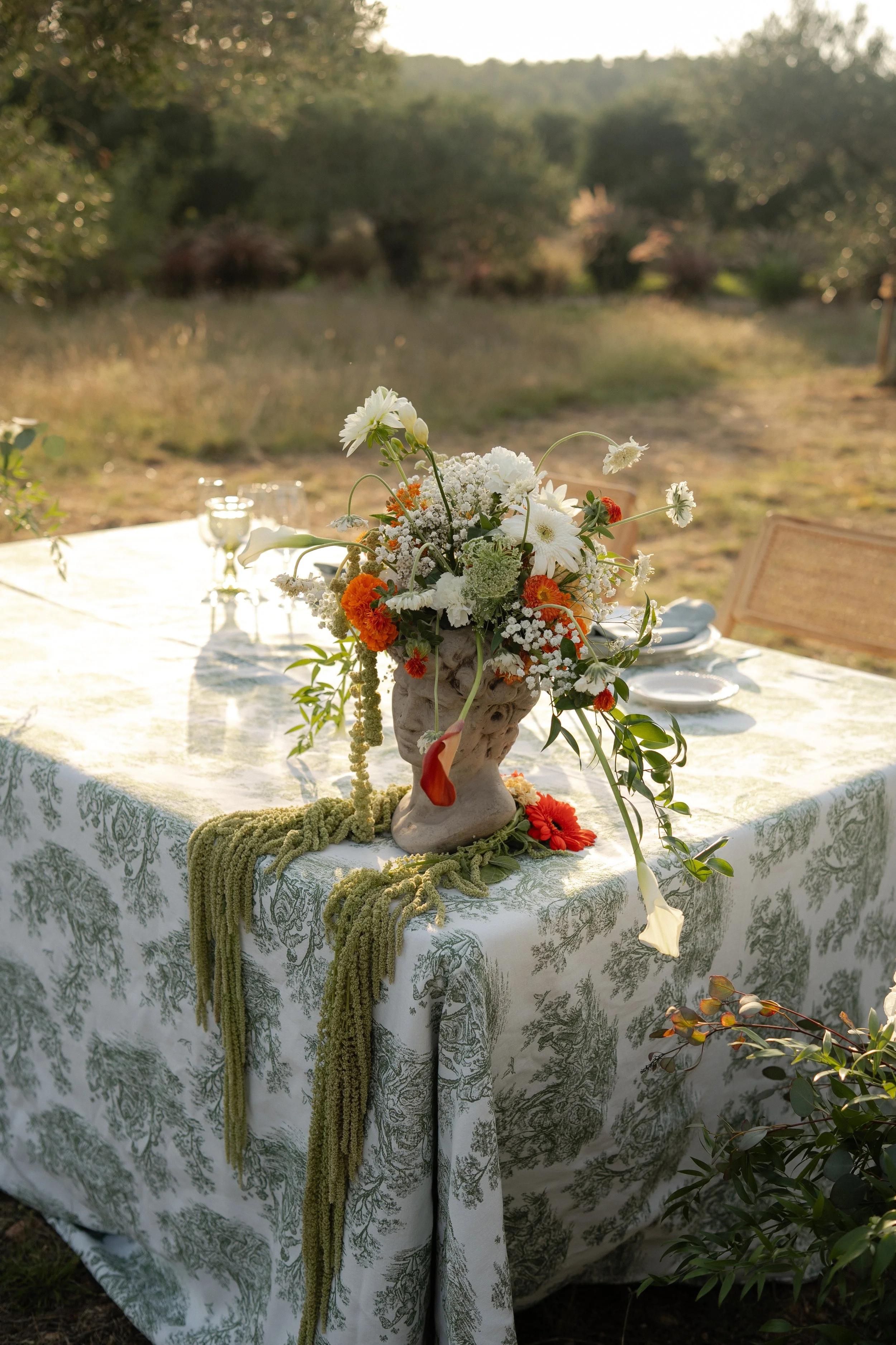 A wedding table set outdoors with a floral centerpiece in a garden or natural setting at sunset in Mas Terrats (Pontós, Girona).