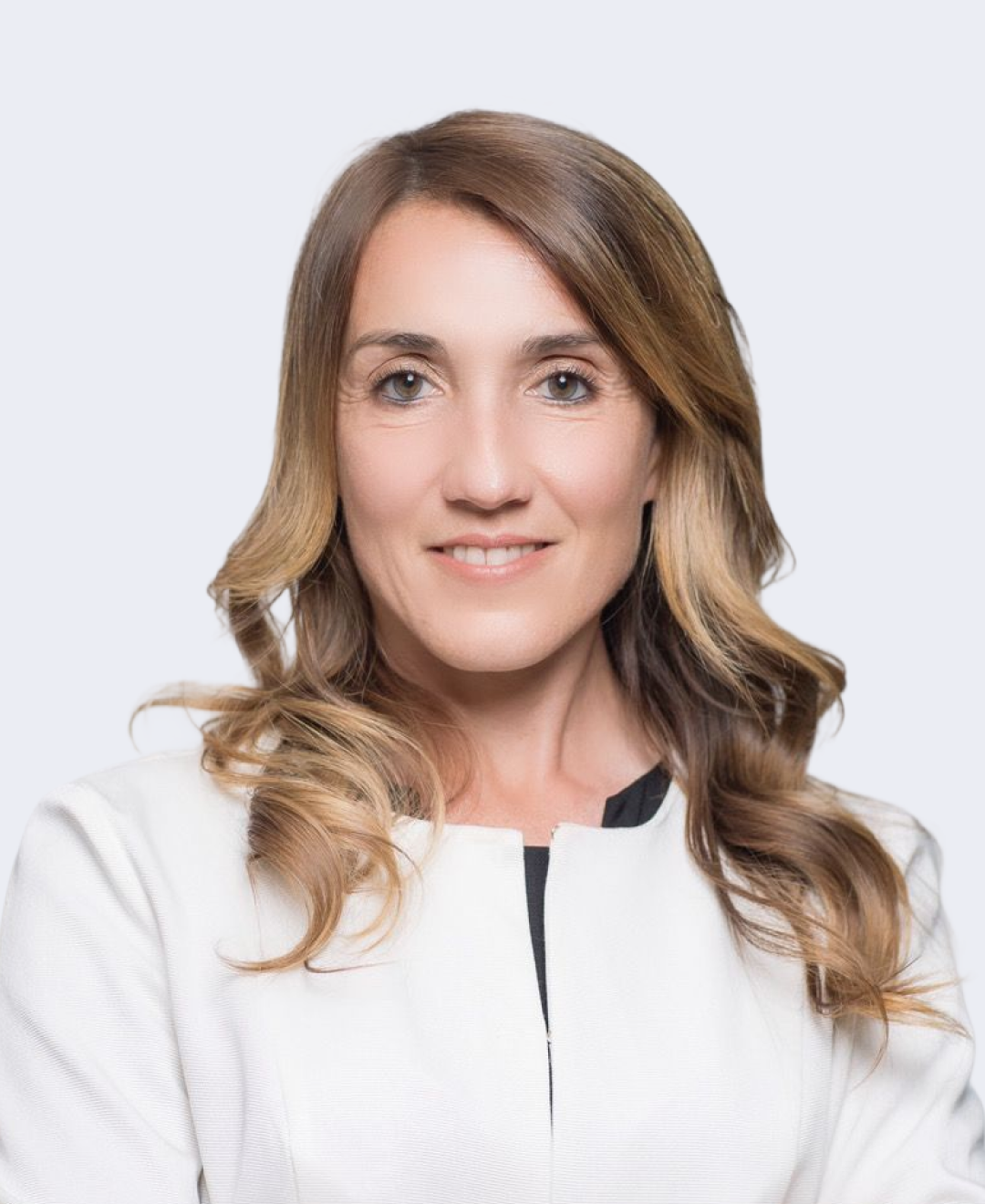 Headshot of a woman with long, wavy light brown hair wearing a white blazer against a plain light grey background.