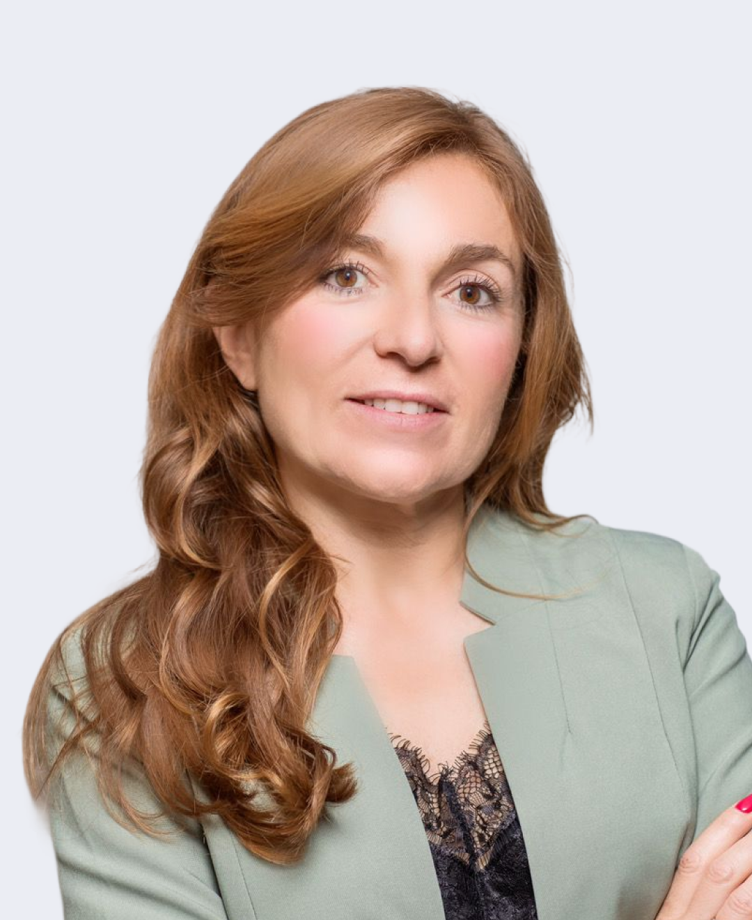A woman with long, wavy, auburn hair wearing a light green blazer over black lace top, posing against a light gray background.