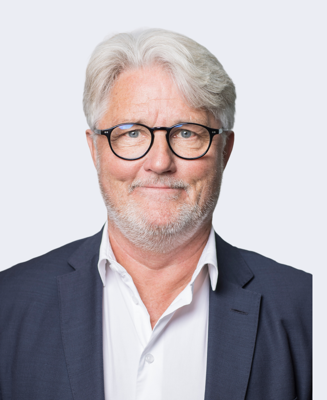 A headshot of an older man with gray hair, glasses, and a beard, dressed in a business suit, against a plain light gray background.