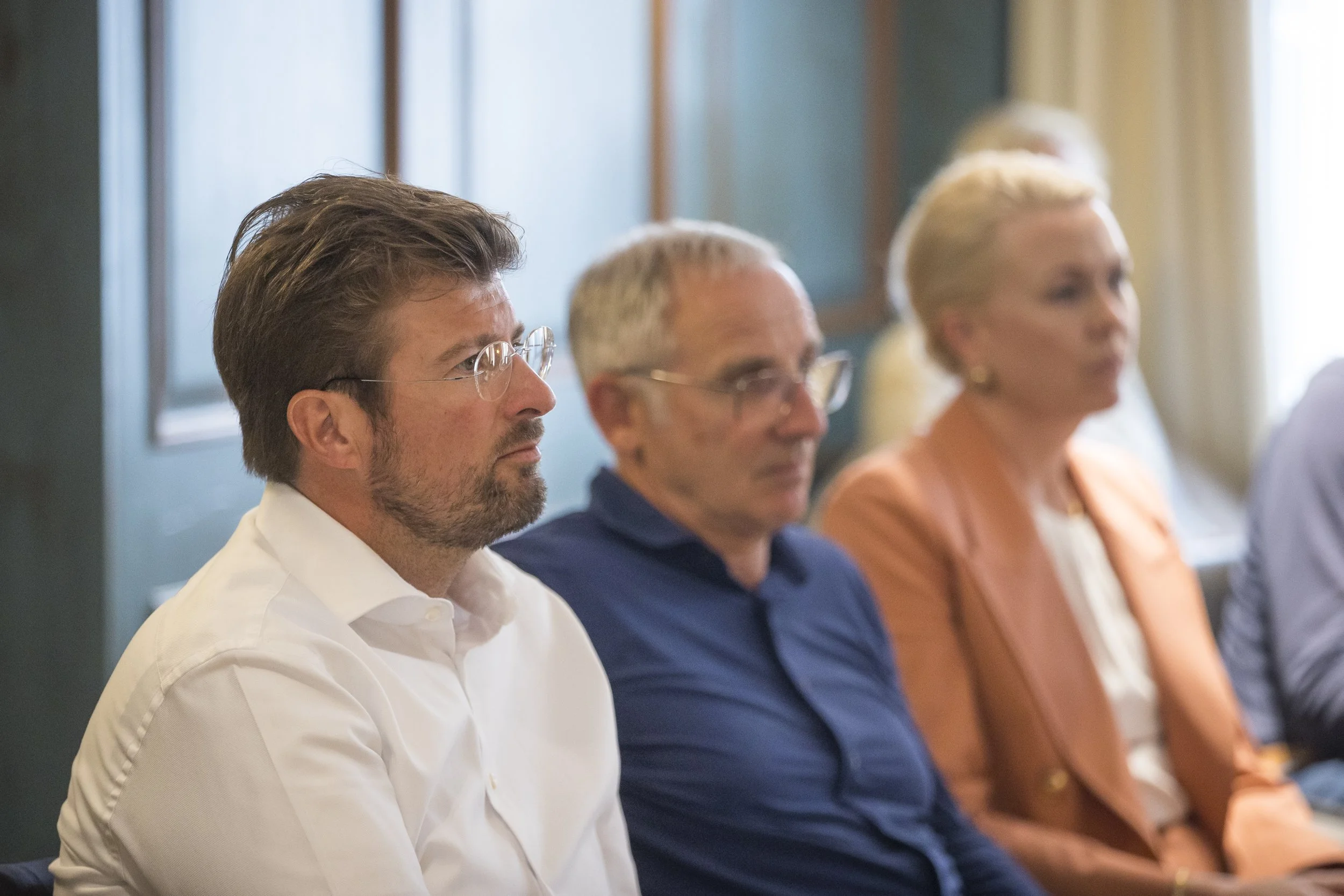 A group of professionals seated in a conference room, listening attentively.