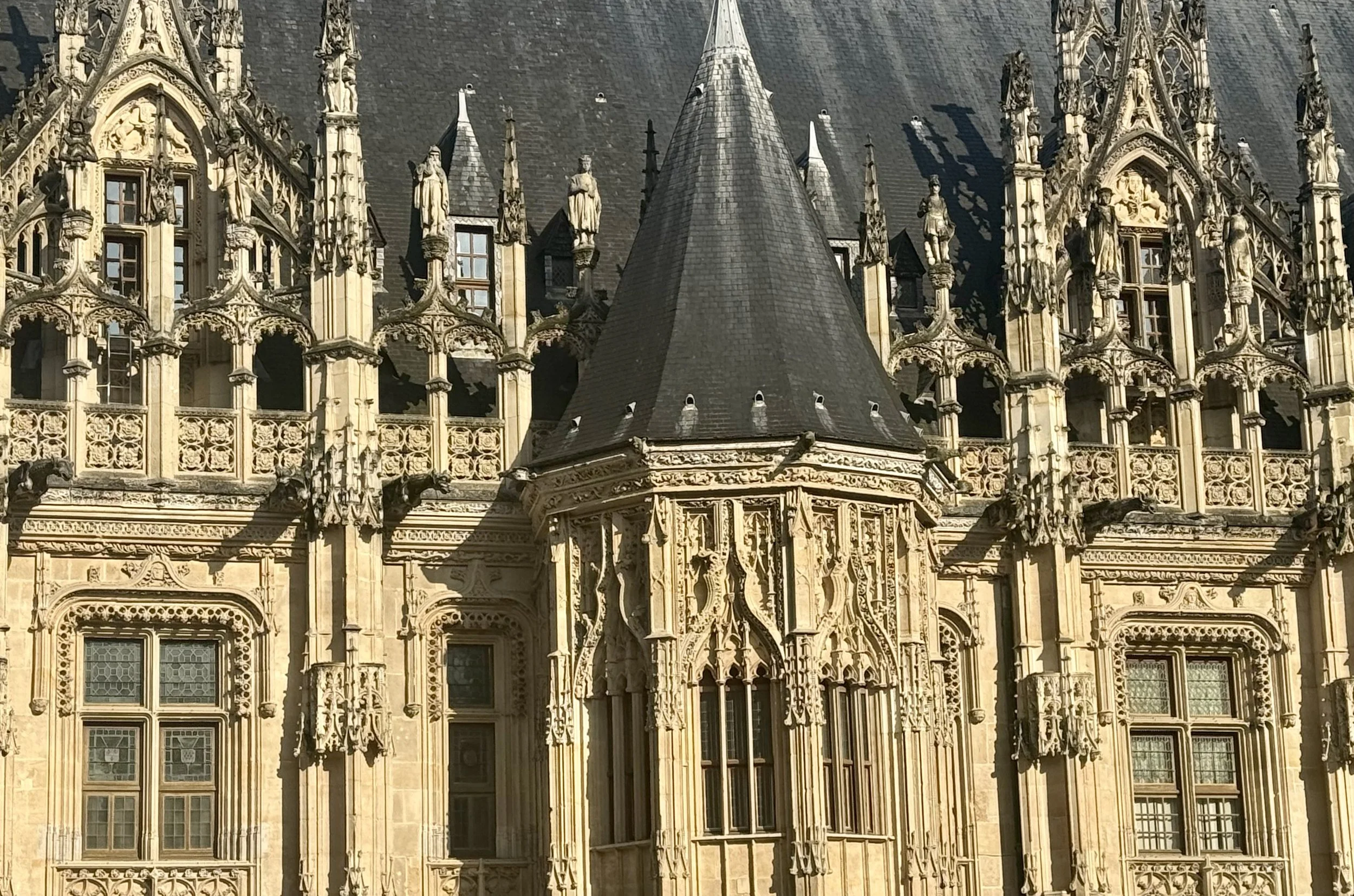 Une façade d'un bâtiment historique en architecture gothique avec de nombreuses sculptures, statues et détails ornementaux, notamment des fenêtres en pierre et un toit en pente.