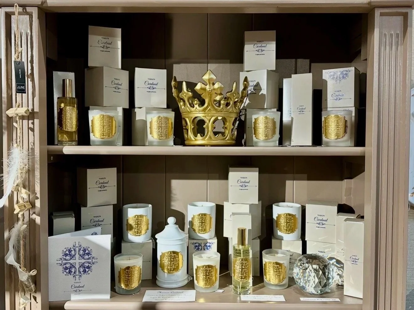 Étagère contenant des bougies, un flacon de parfum, et une décoration en forme de couronne dorée, avec des boîtes et emballages blancs et or