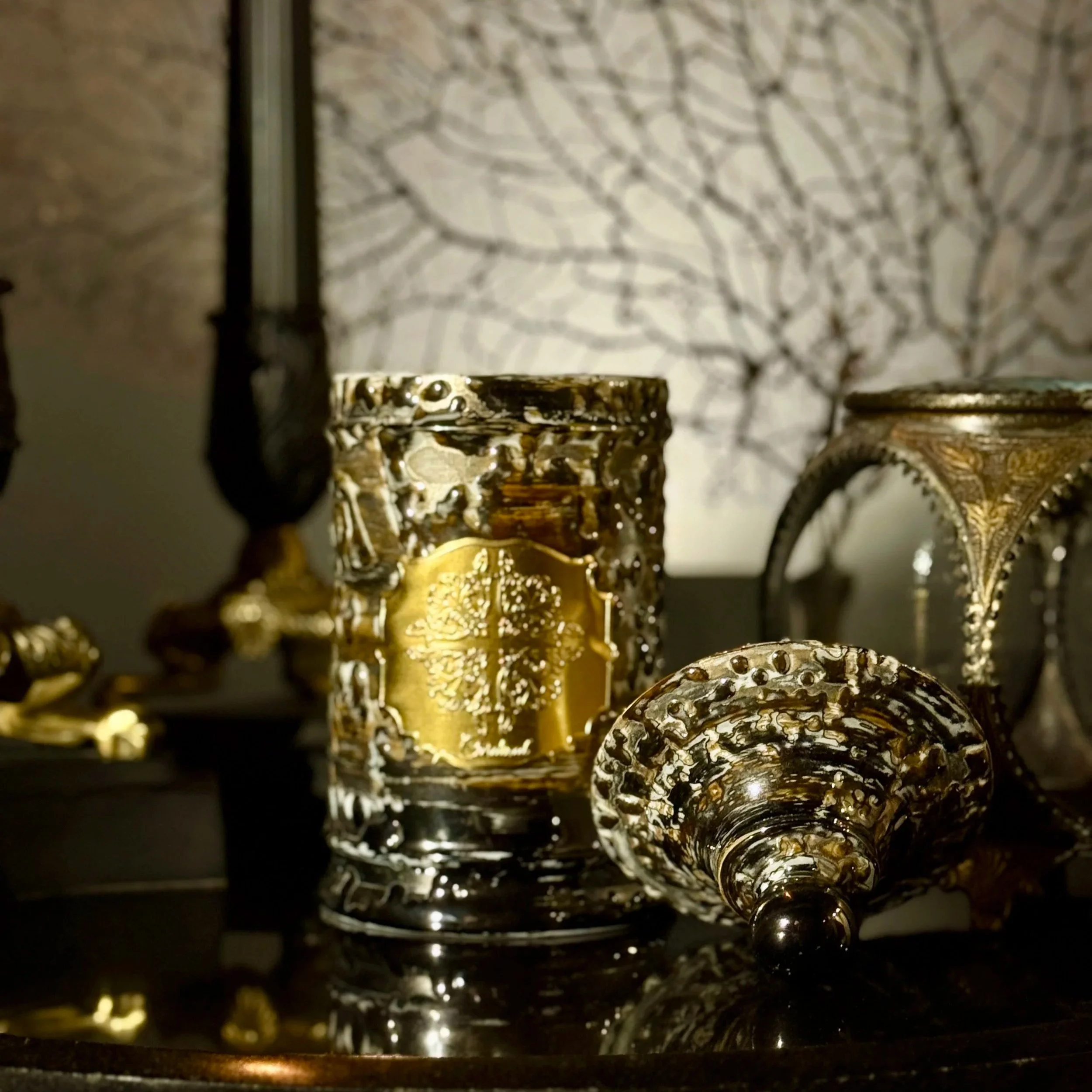 Une rangée de verres en métal doré avec des motifs élaborés, vue de dessous, avec un arrière-plan flou de branches d'arbres sans feuilles sur un mur clair.