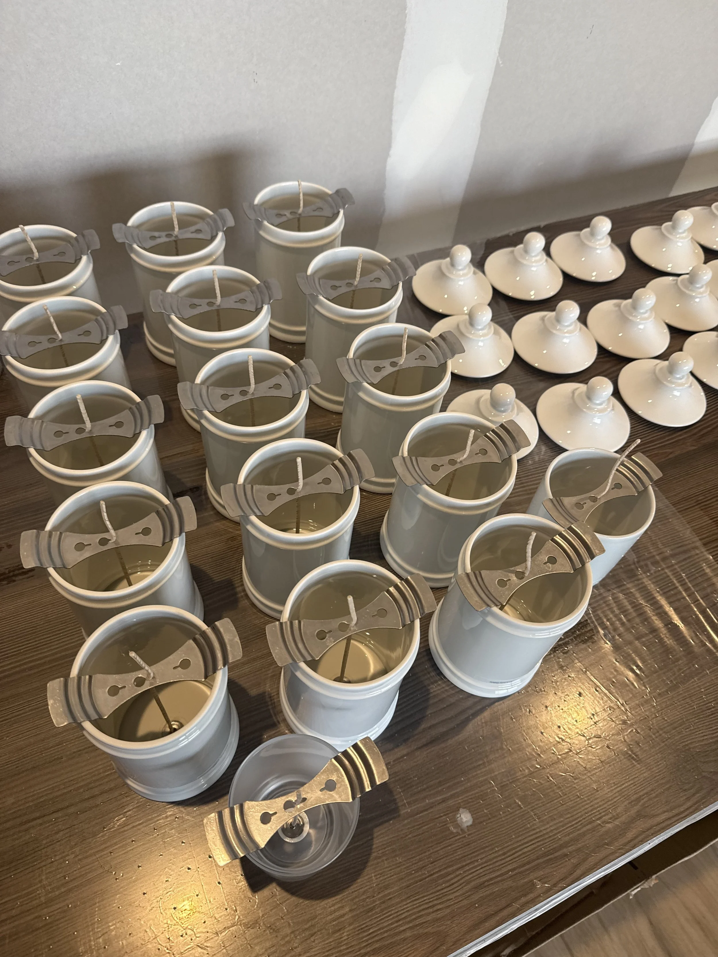 Plusieurs petits pots en céramique blanc sont disposés sur une table en bois, certains avec un couvercle, probablement des bougies ou des savons.