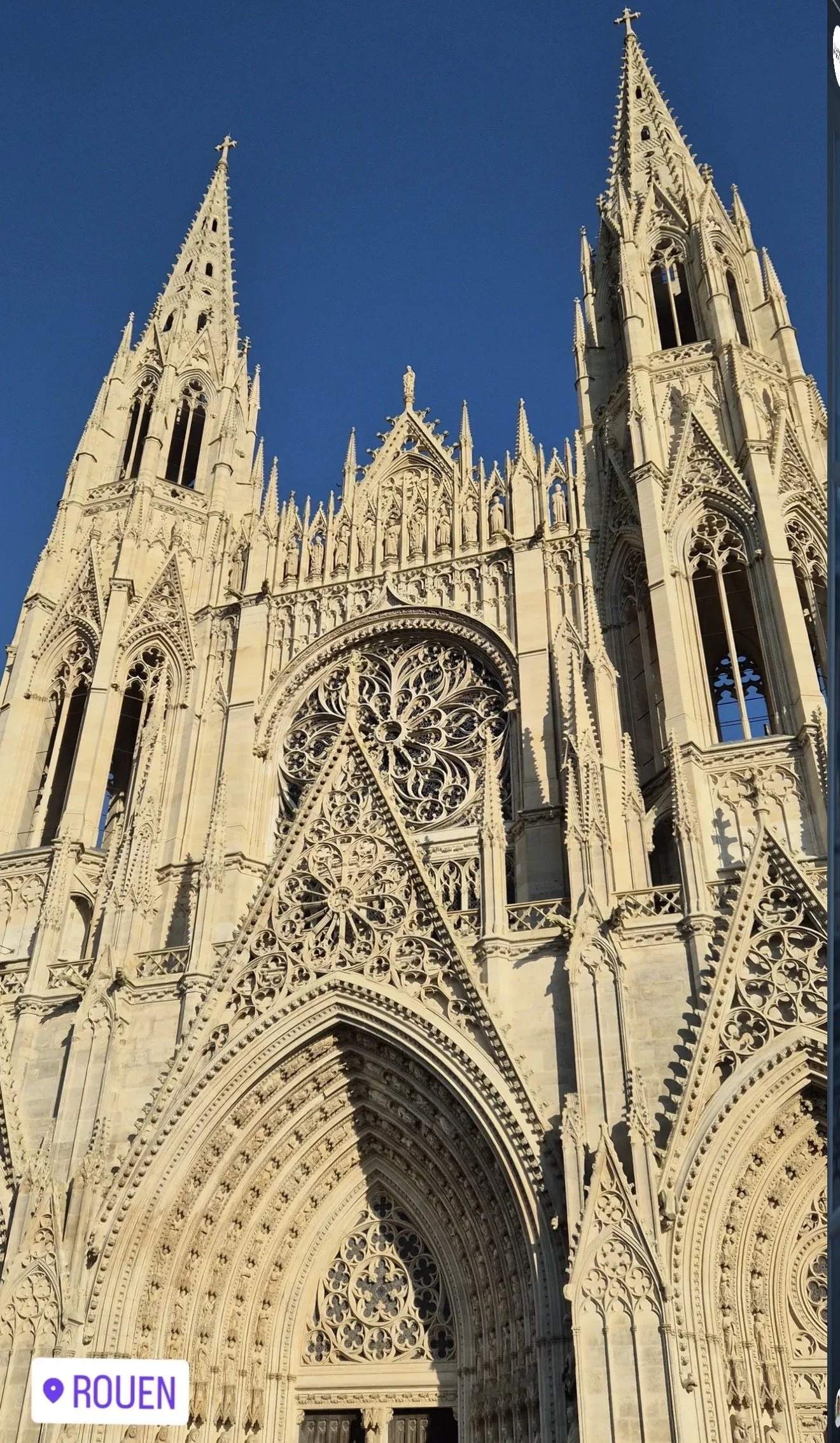 Une cathédrale gothique avec des flèches pointues, des sculptures élaborées, une rosace en pierre et un portail décoré dans un style architectural détaillé.