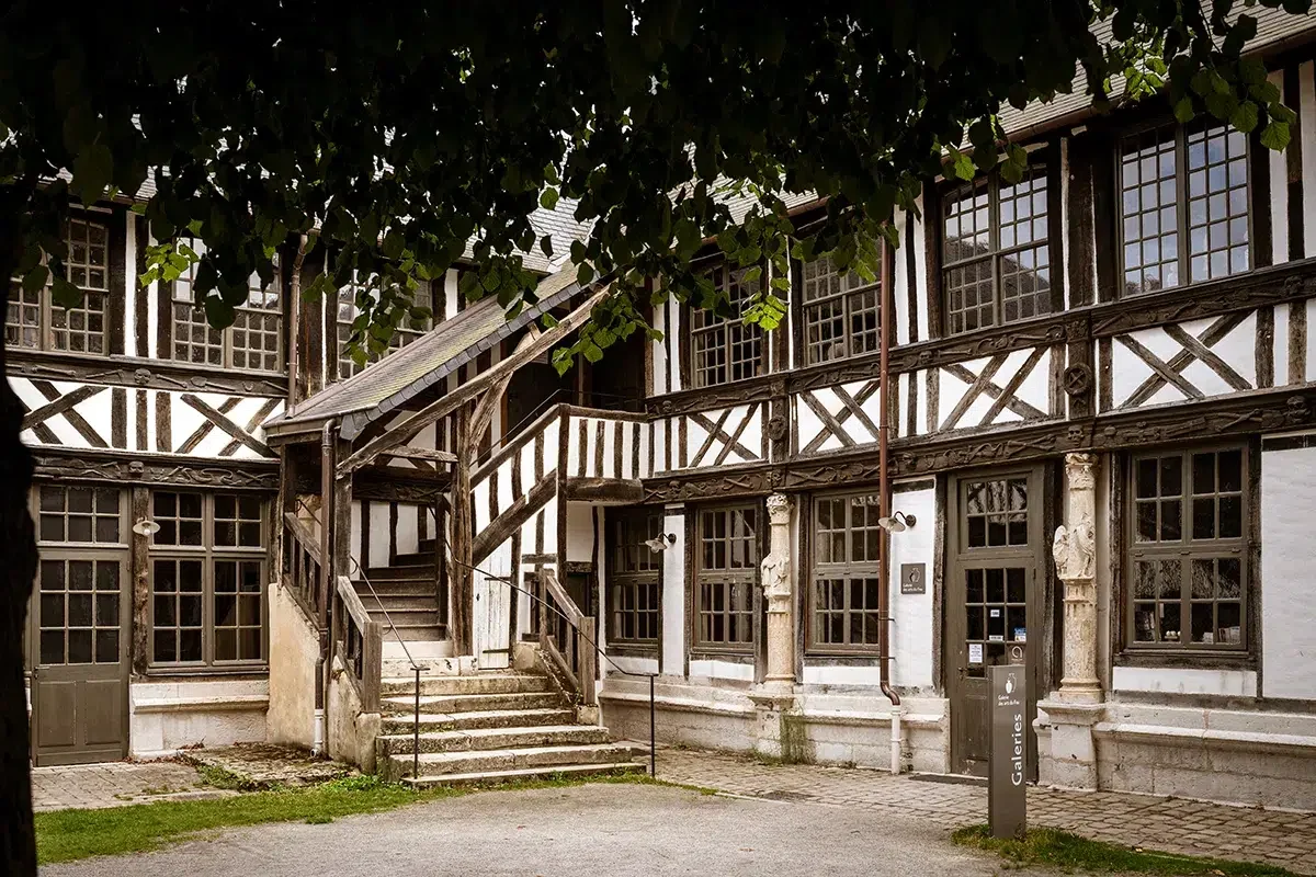 Une vieille maison à colombages avec un escalier en pierre, des fenêtres à petits carreaux et une signalisation indiquant 'Galerie'.