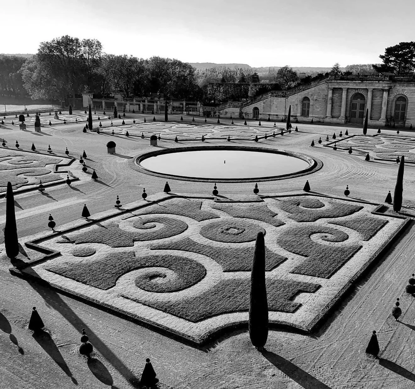 Jardin ornemental enneigé avec des motifs géométriques, un bassin central et des arbres en arrière-plan.