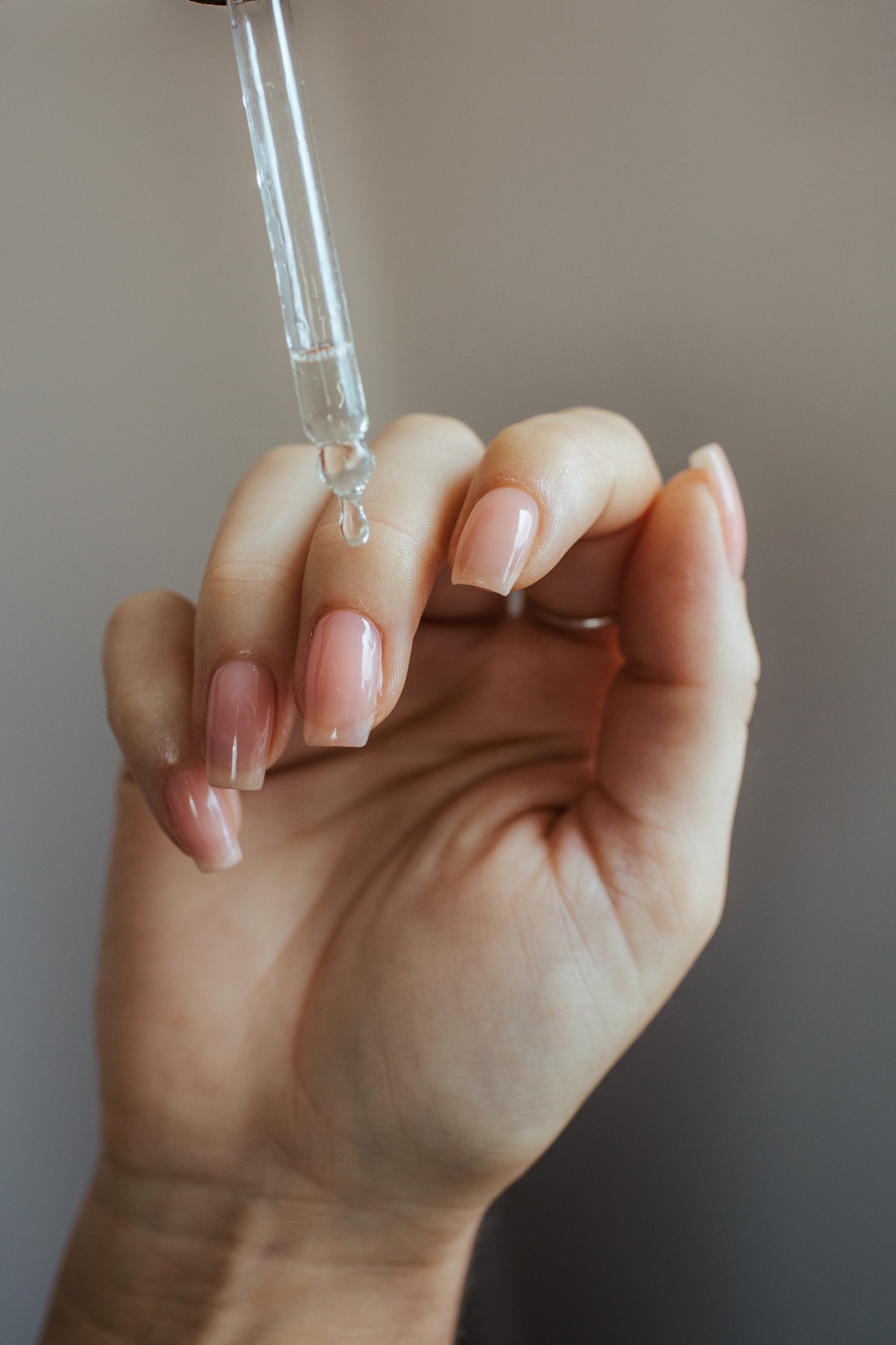 A hand holding a glass dropper with clear liquid, positioned over the index finger.