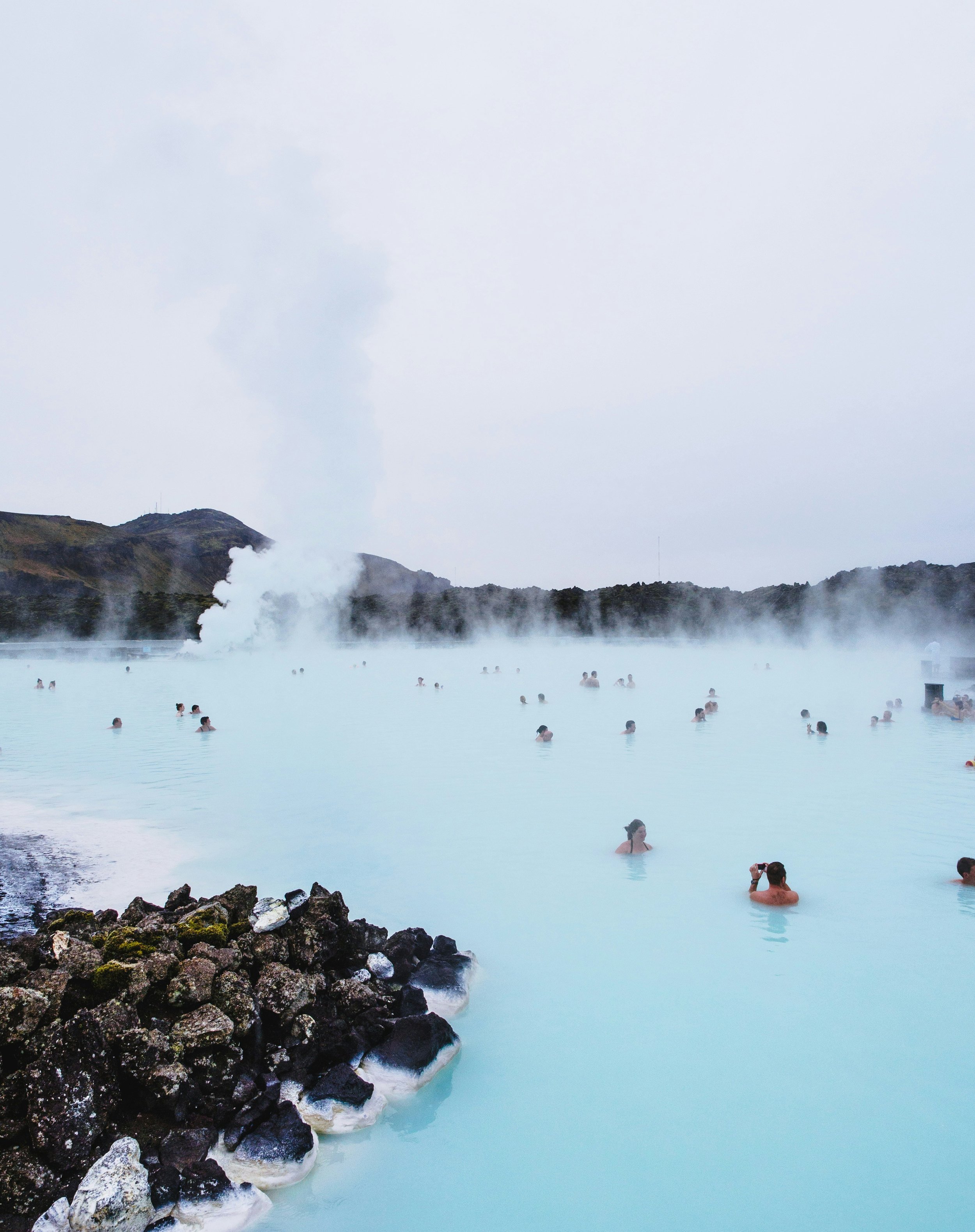 People bathing in the Blue Lagoon, a geothermal spa in Iceland, surrounded by steam and rocky landscape.