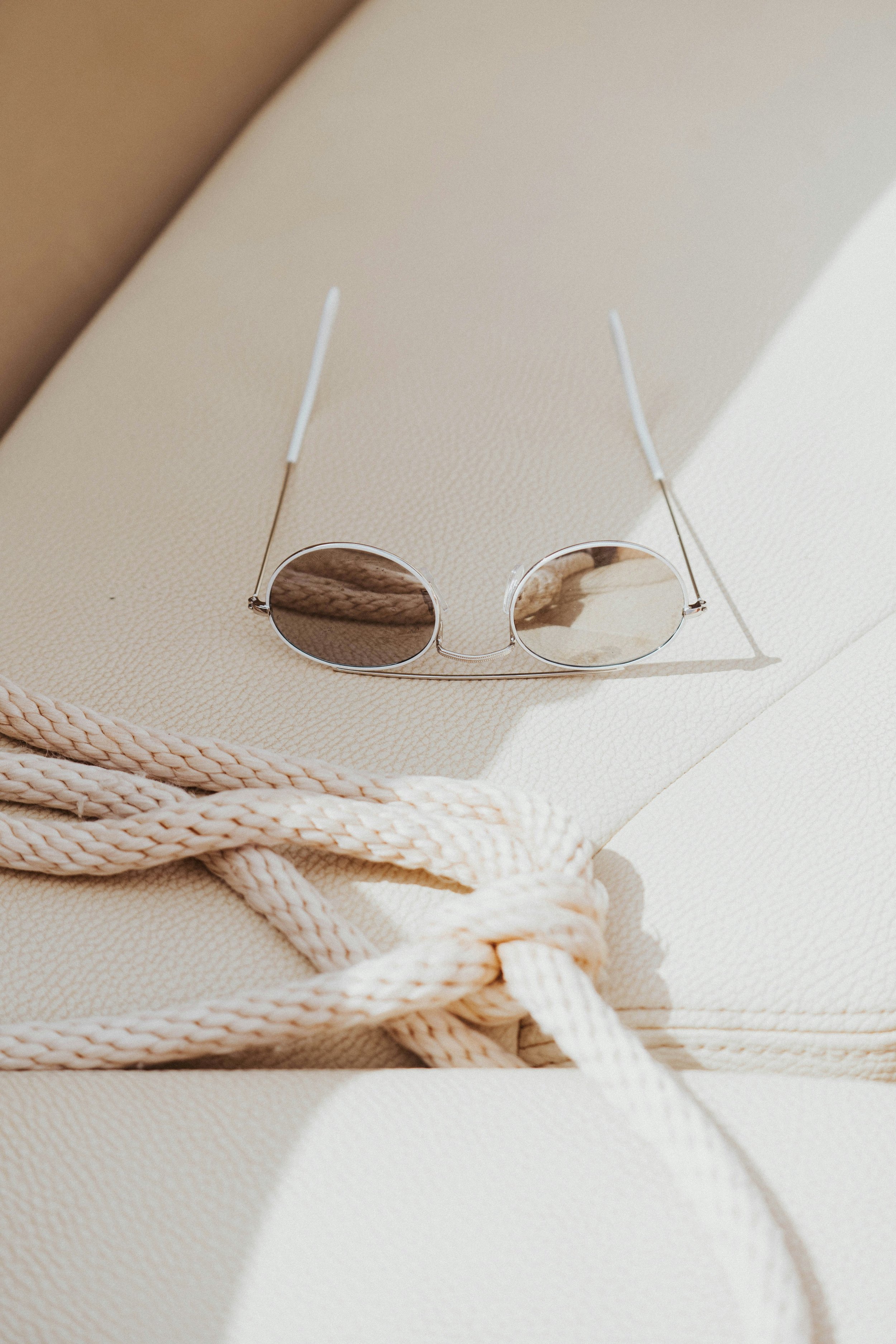 Round sunglasses and a knotted rope on a white, textured surface.