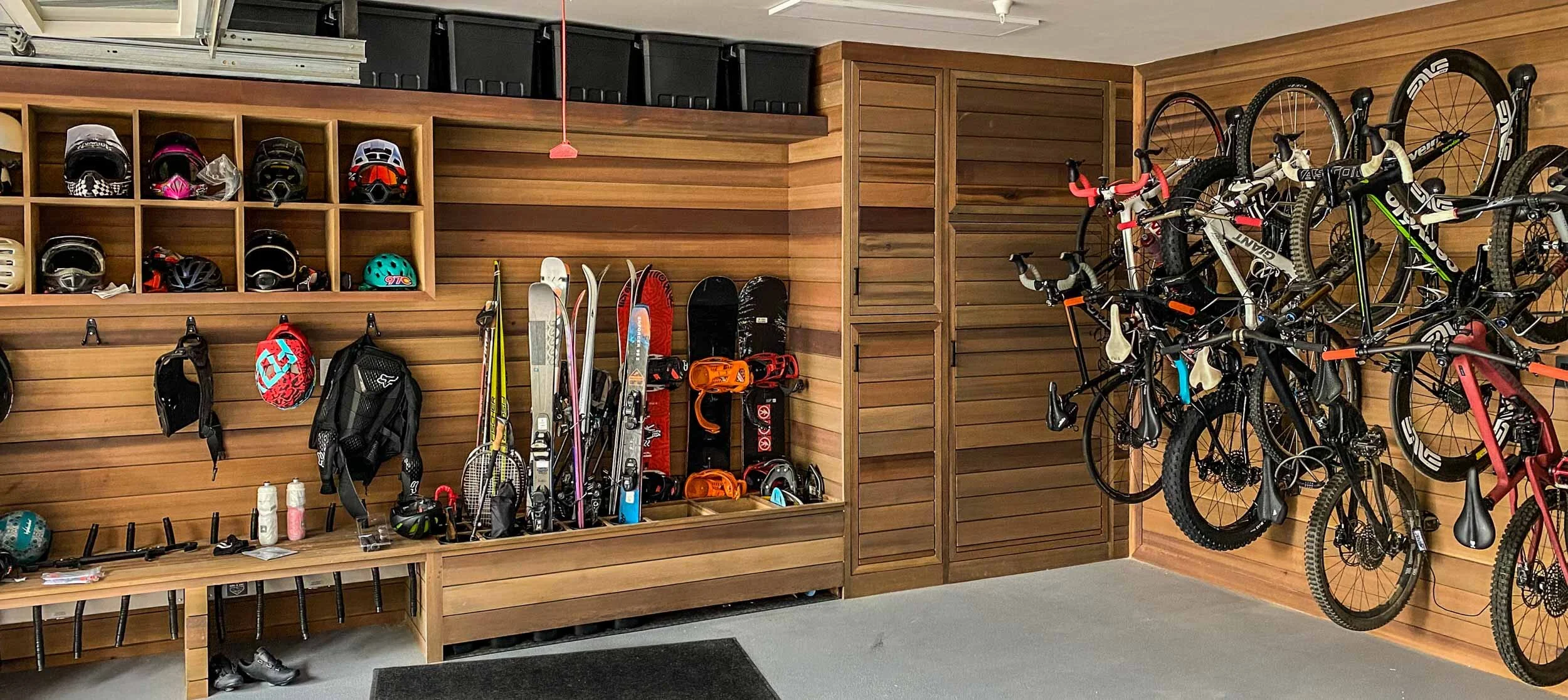 A garage with wooden paneling filled with sports gear including helmets, bikes, skis, and accessories organized on shelves and racks.