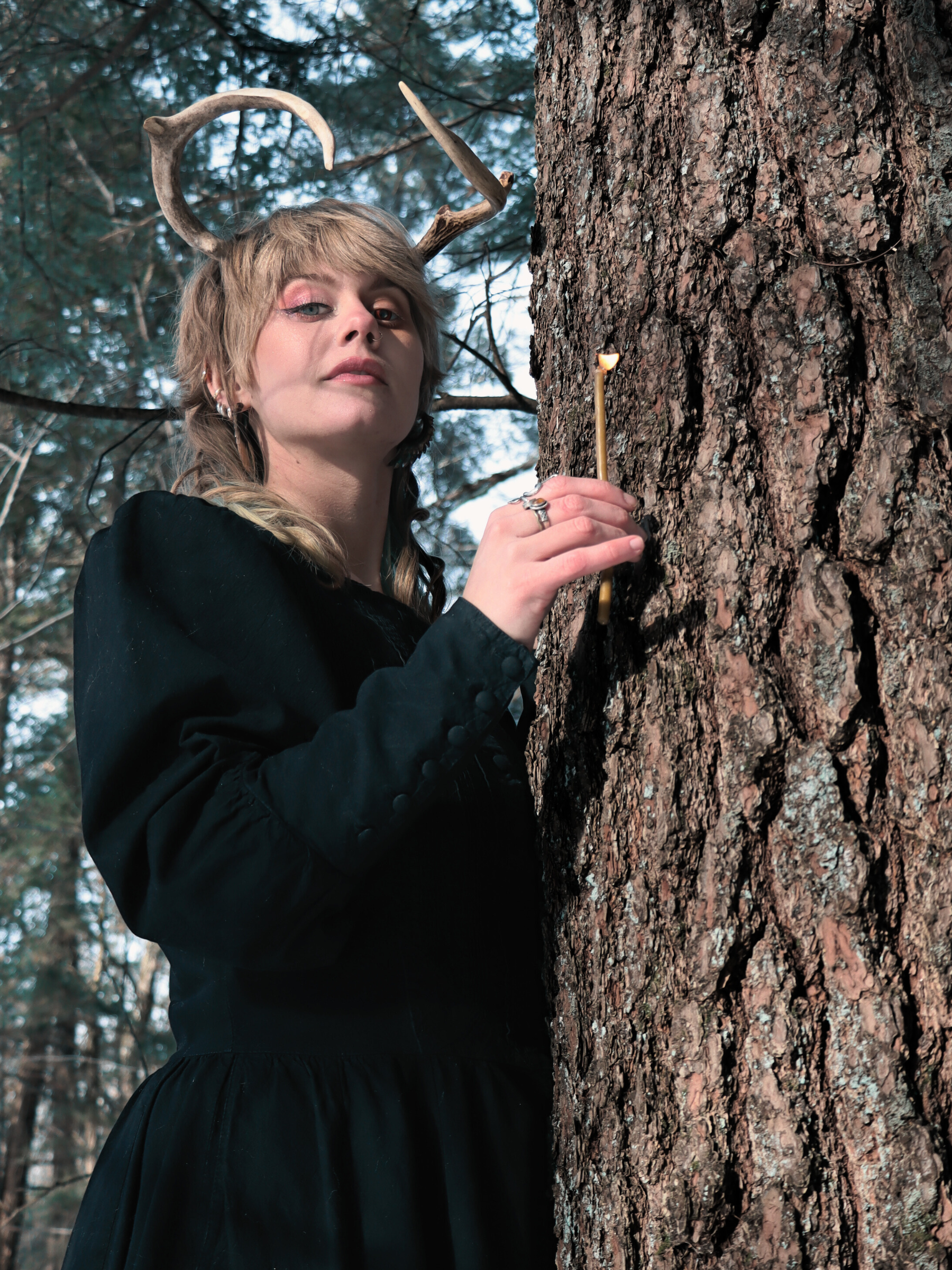 jordann funk with satyr horns holding a candle next to hemlock tree