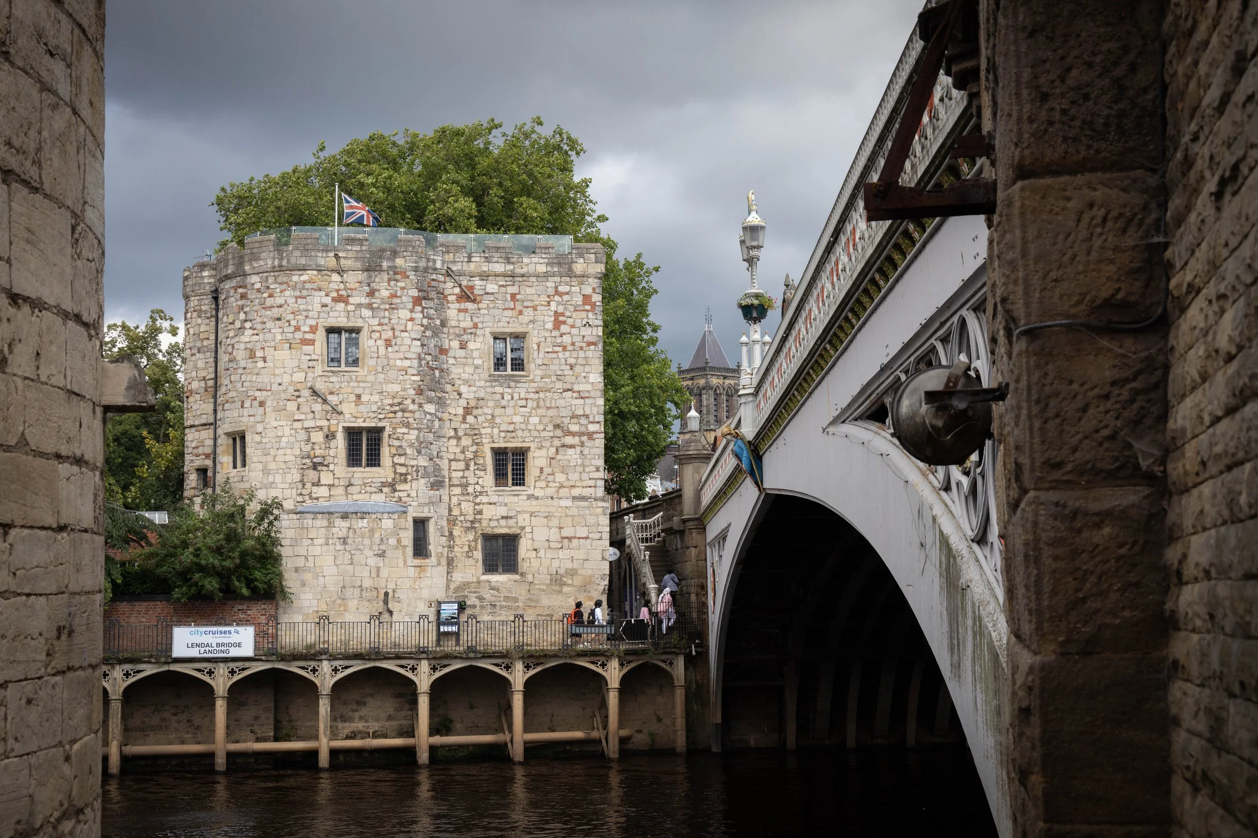 View of Lendal Bridge in York, England, with historic buildings, a river, and a cloudy sky.