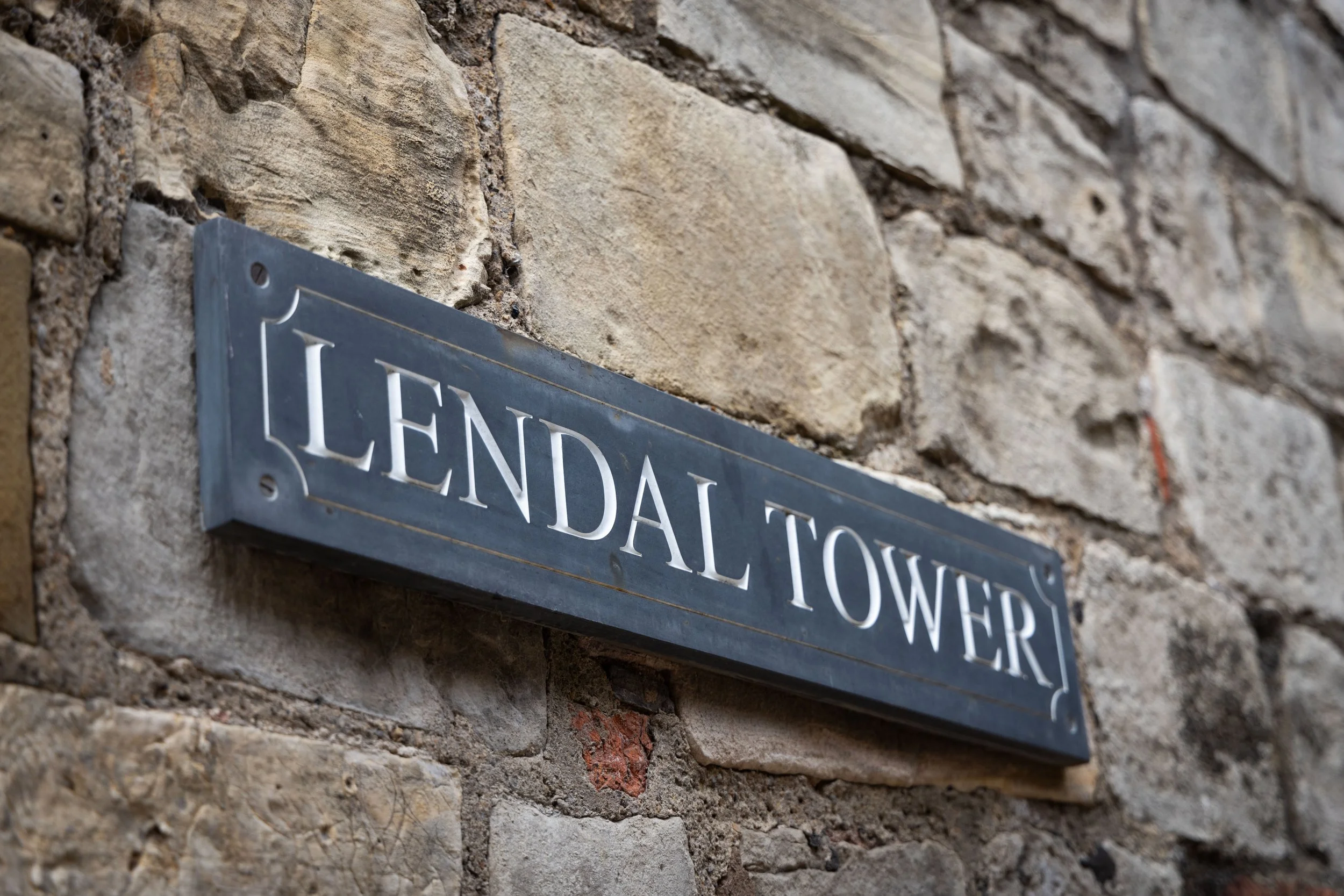 Close-up of a metal street sign attached to a brick wall, partially reading 'LENDAL TOWED'.