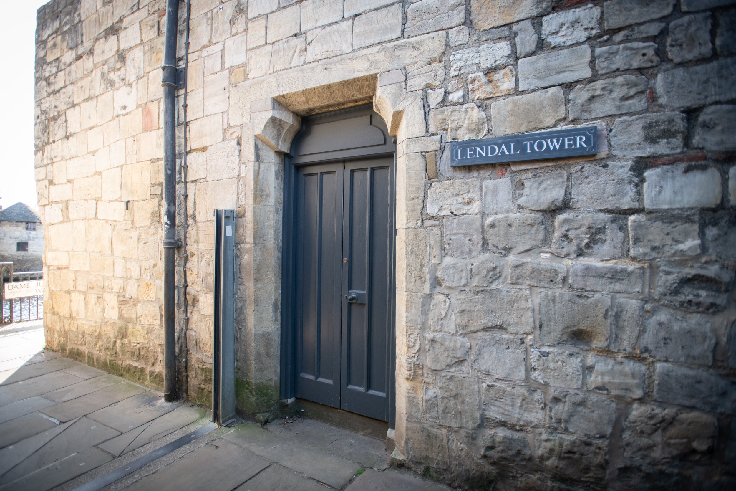 Stone building wall with a door labeled 'Lendal Tower' and a black pipe running down the side.