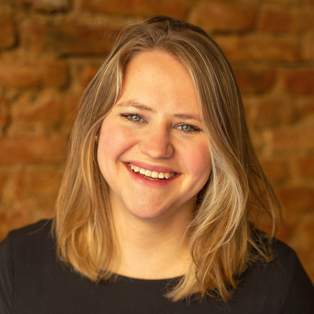 Nahaufnahme einer lachenden jungen Frau mit blonden Haaren gegen eine Ziegelsteinwand