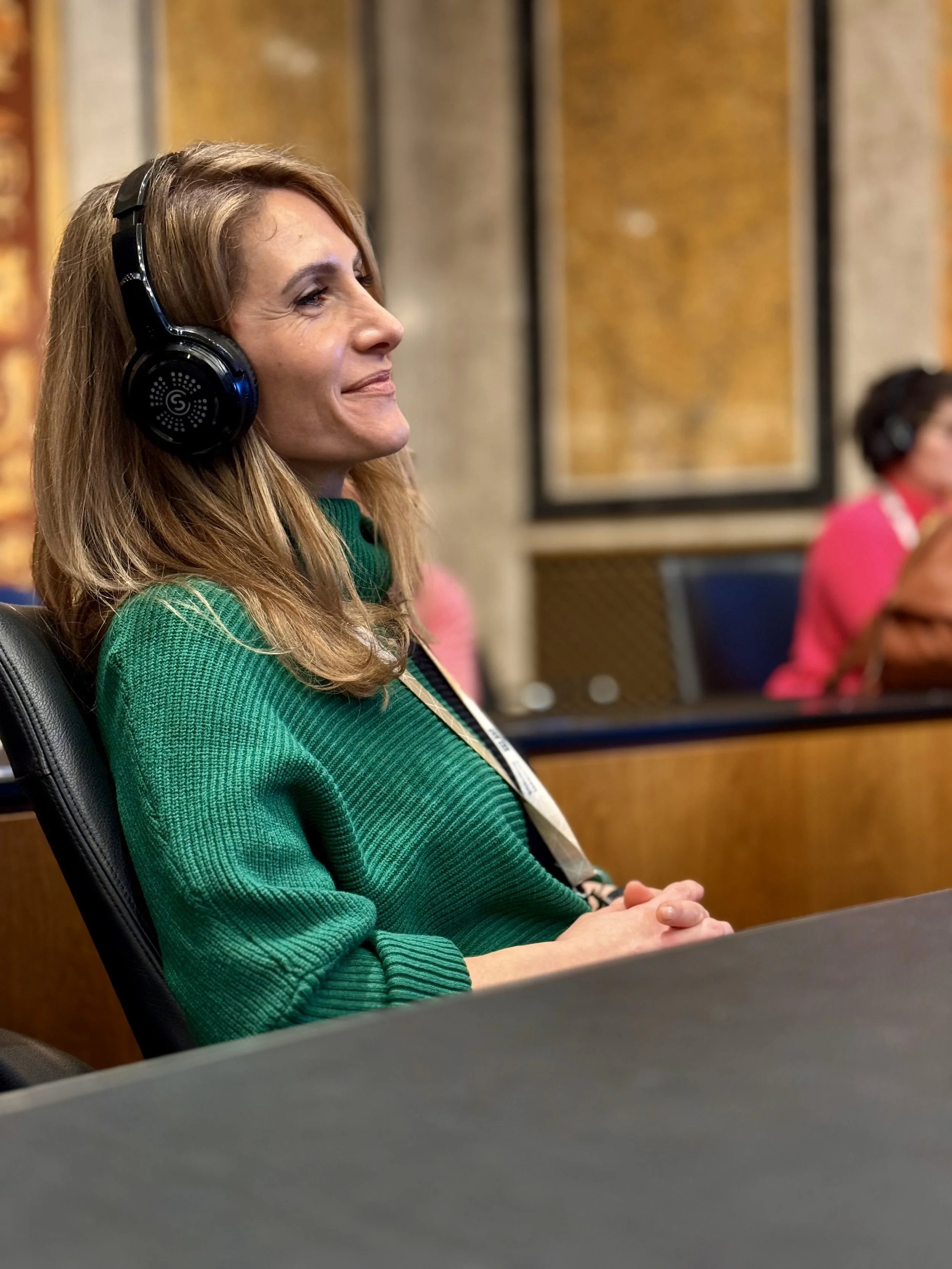 Frau trägt ein grünes Kleid und Kopfhörer, sitzt im Konferenzraum.