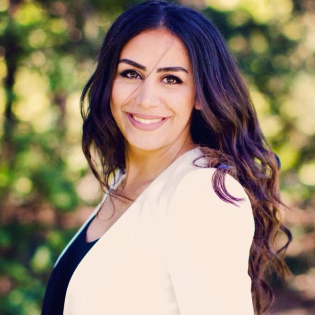 Lächelnde Frau mit dunklem, lockigem Haar und hellgrünem Hintergrund.