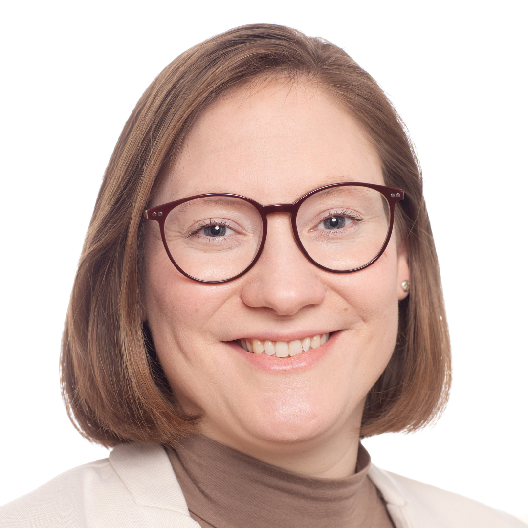 Nahaufnahme einer lächelnden Frau mit braunen Haaren, trägt Brille und beige Kleidung vor weißem Hintergrund.