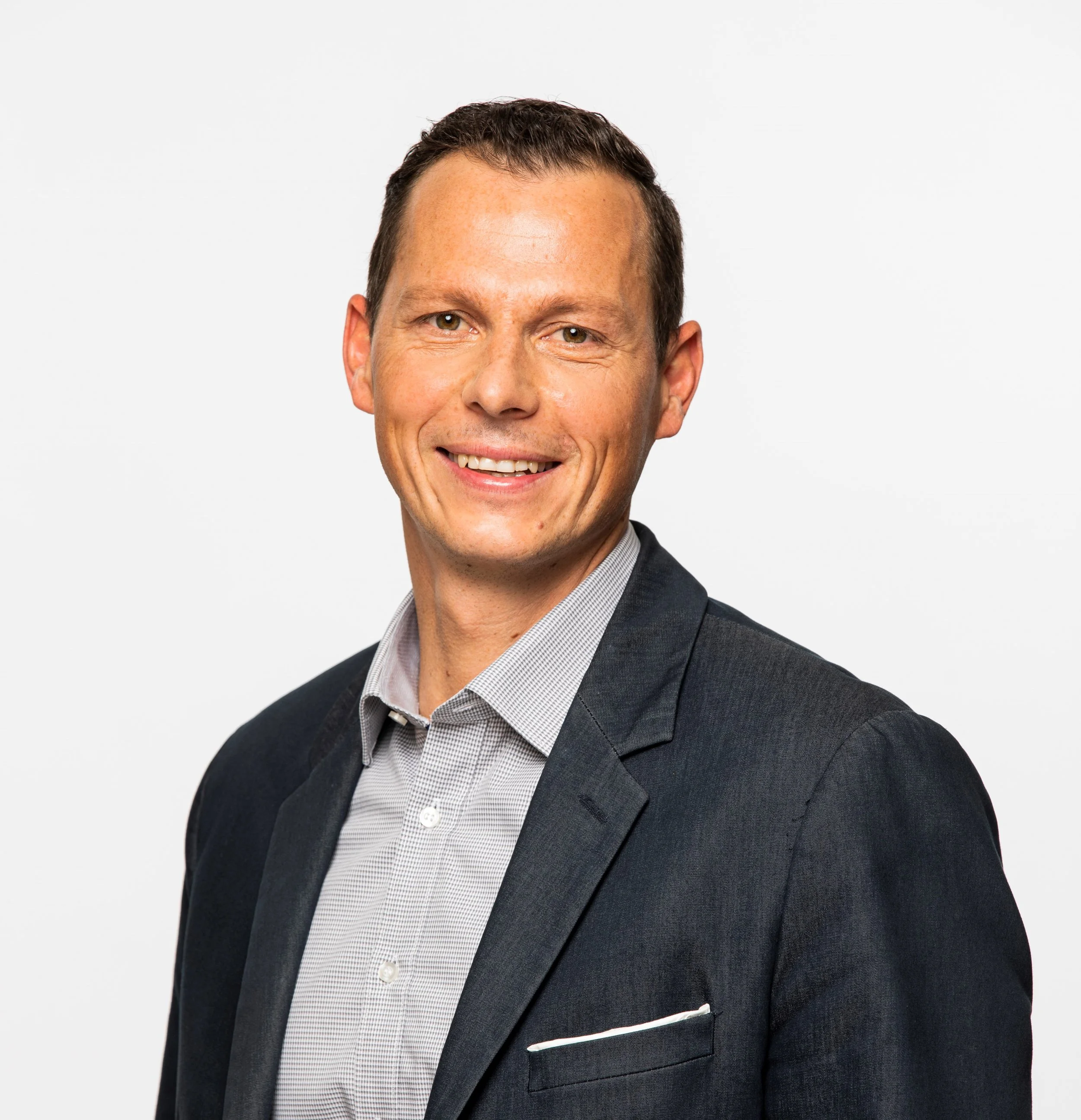 Porträt eines lachenden Mannes in formeller Kleidung vor weißem Hintergrund.