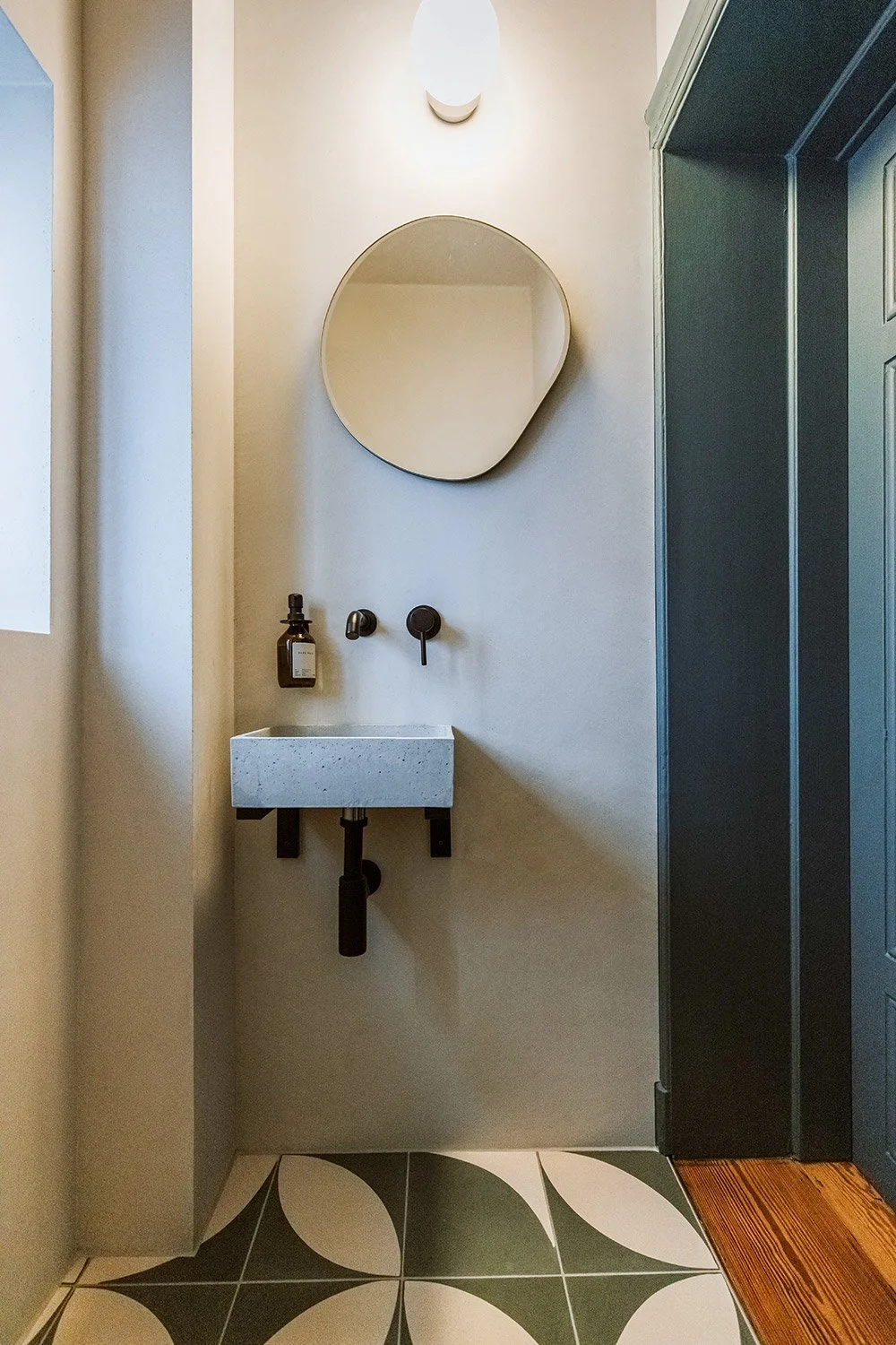 Kleiner Waschbecken mit dunklem Hahn und Wandspiegel in einem modernen Badezimmer, graue Wand, dunkles Türrahmen, gestrichener Holzboden