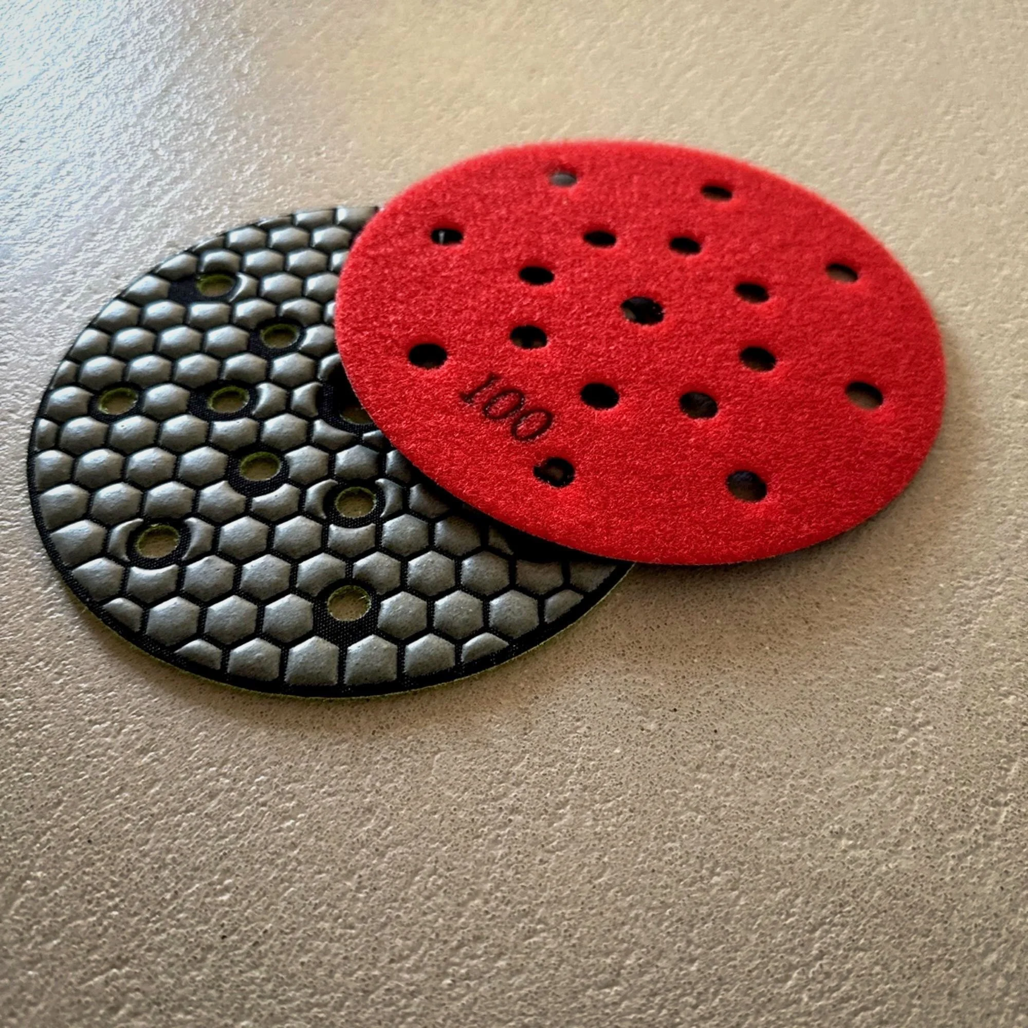 Zwei Schleifscheiben, eine rot und eine schwarz, auf einer glatten Oberfläche.