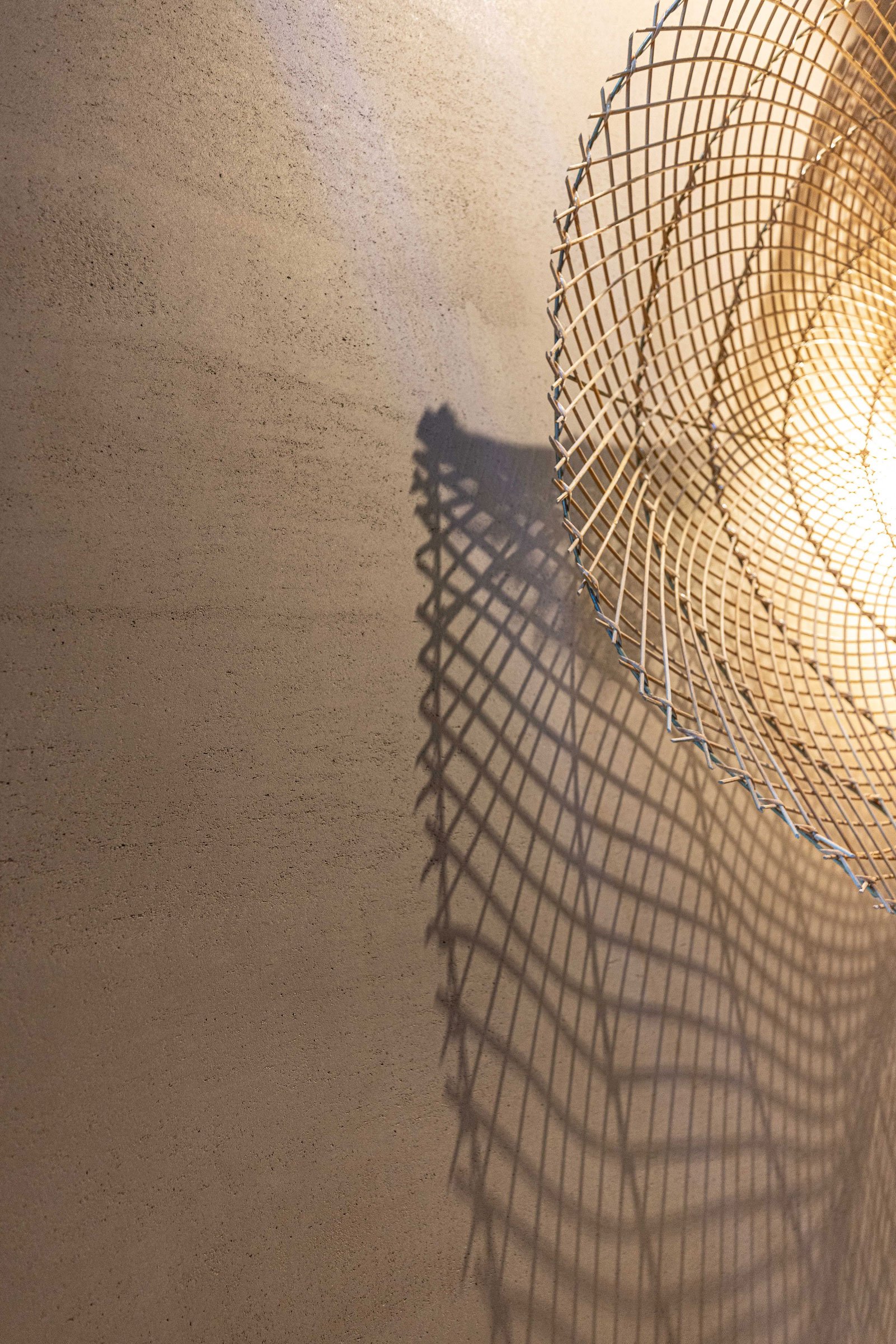 Ein Lampenschirm aus einem Drahtgitter, der an einer Wand hängt, wirft ein schattenreiches Muster an die Wand.