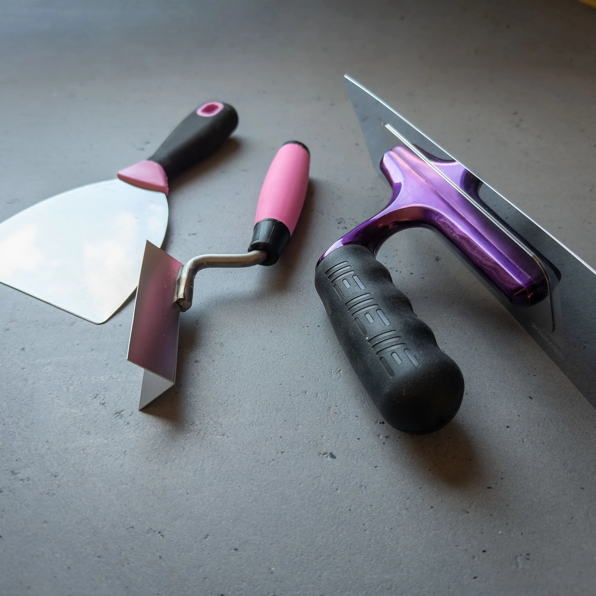 Verschiedene kleine Handwerkzeuge auf einer grauen Oberfläche, darunter einen Kelle, eine Walze und eine Rolle.