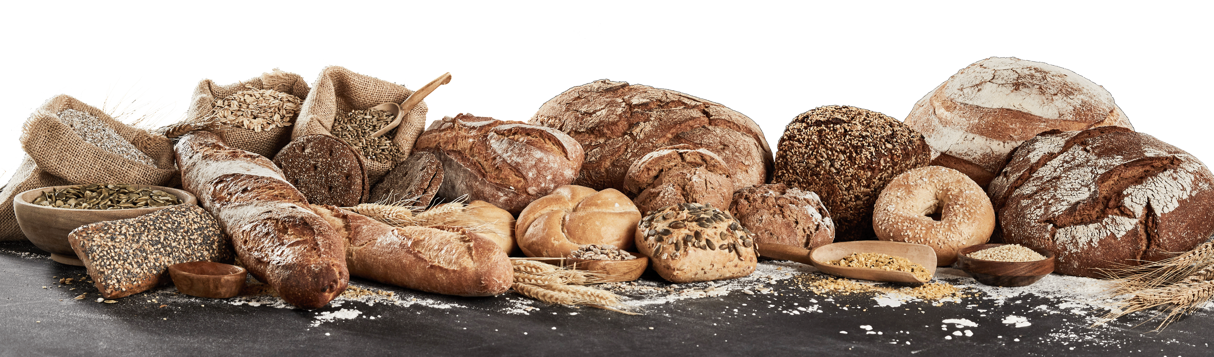 Assorted varieties of bread and baked goods arranged on a surface with scattered flour and grains