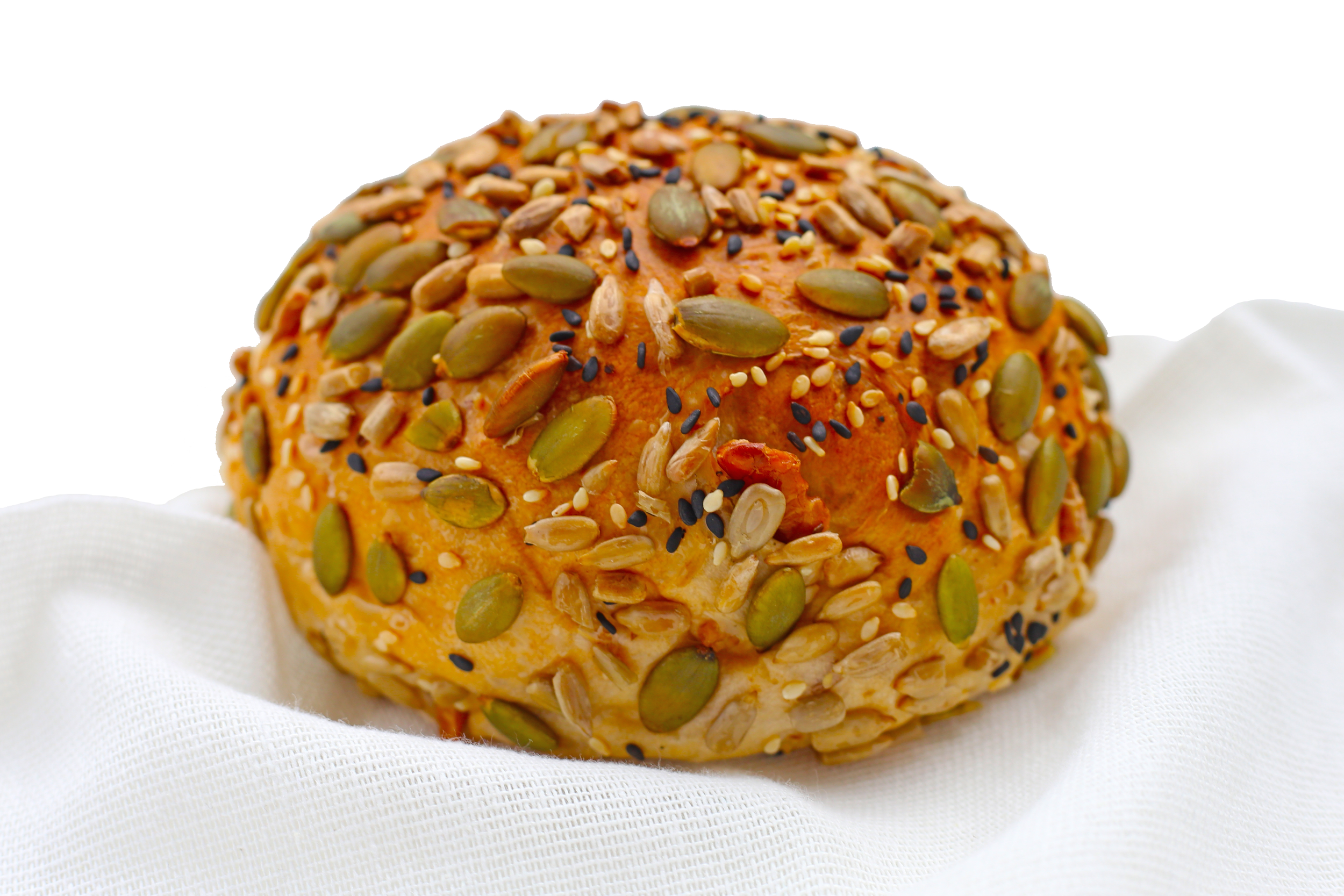 Close-up of a round, orange-colored baked good topped with pumpkin seeds, sesame seeds, and black sesame seeds, resting on a white cloth.