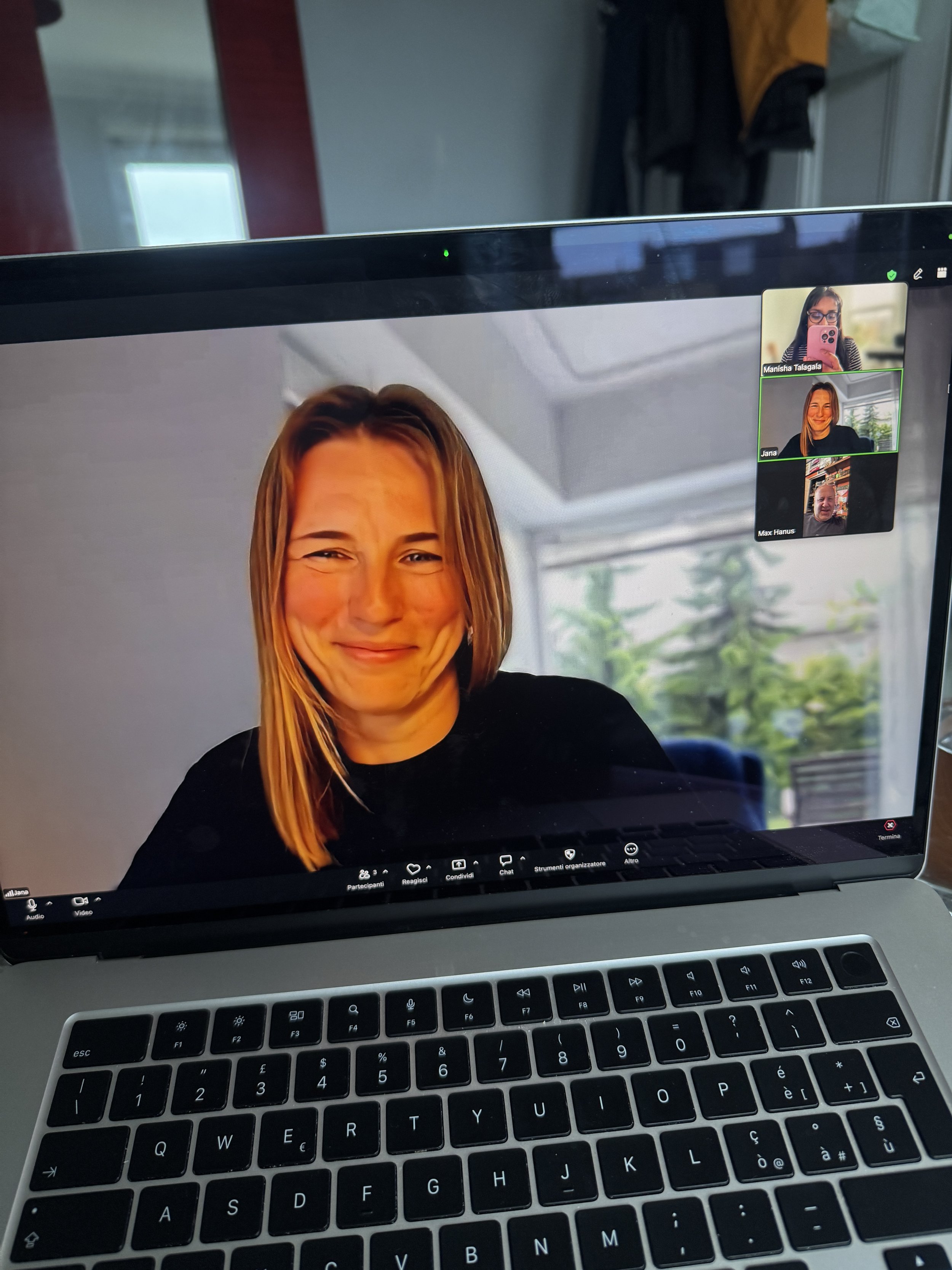 Laptop screen displaying a video call with three participants, including a woman with a large smile, and a keyboard below the screen.