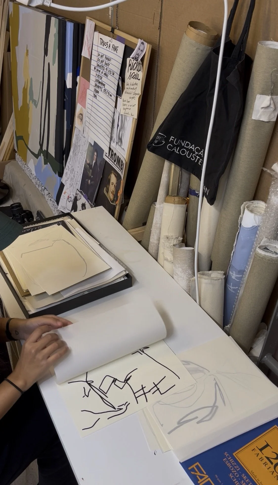 Art studio workspace with drawings, sketches, rolled canvases, and reference images on a table and wall. Artwork by © 2026 Aura Delamotte Barrera, All rights reserved.