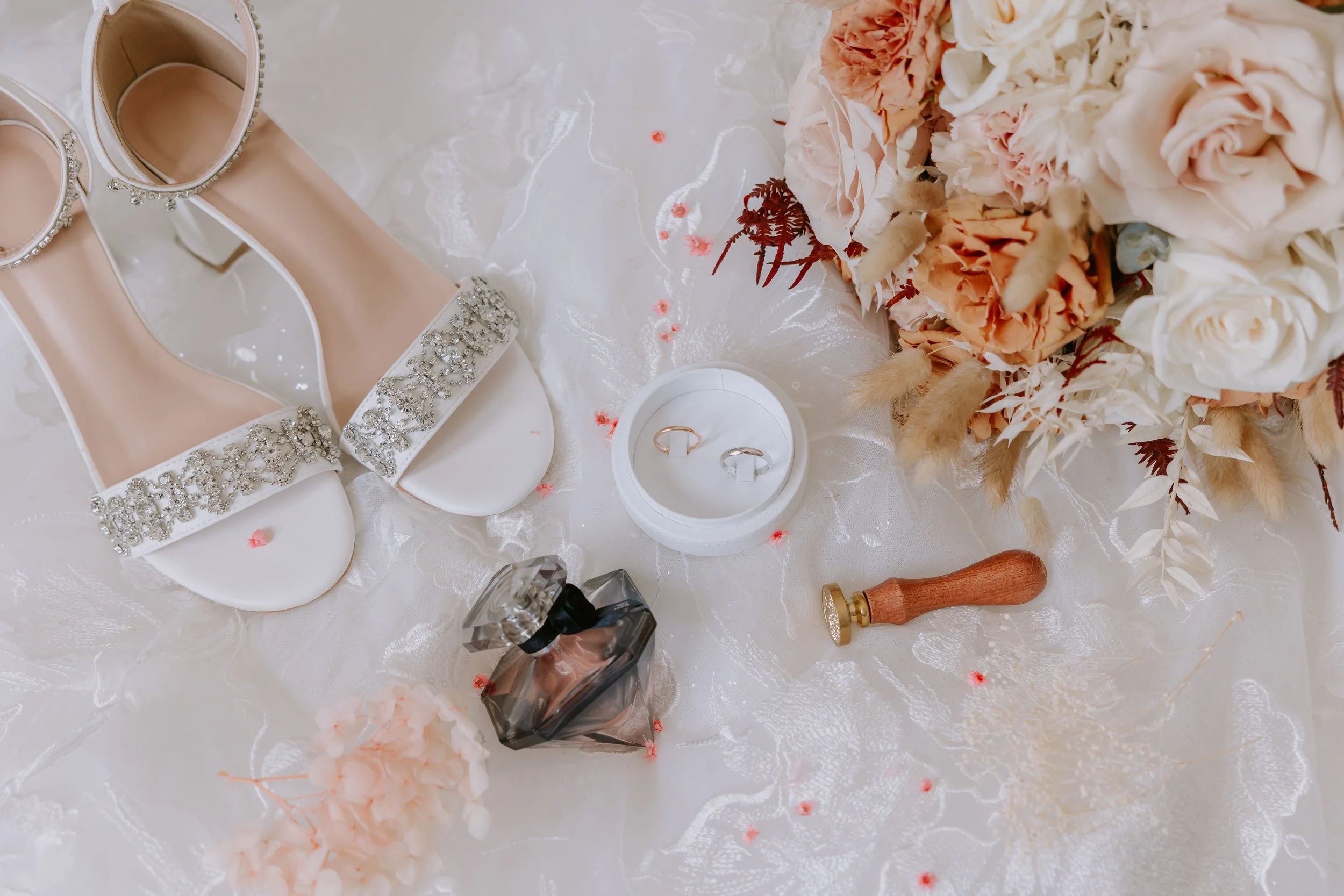 Chaussures de mariage à talons hauts, ornées de bijoux, décorées de strass, sur une table avec des fleurs et des bagues.