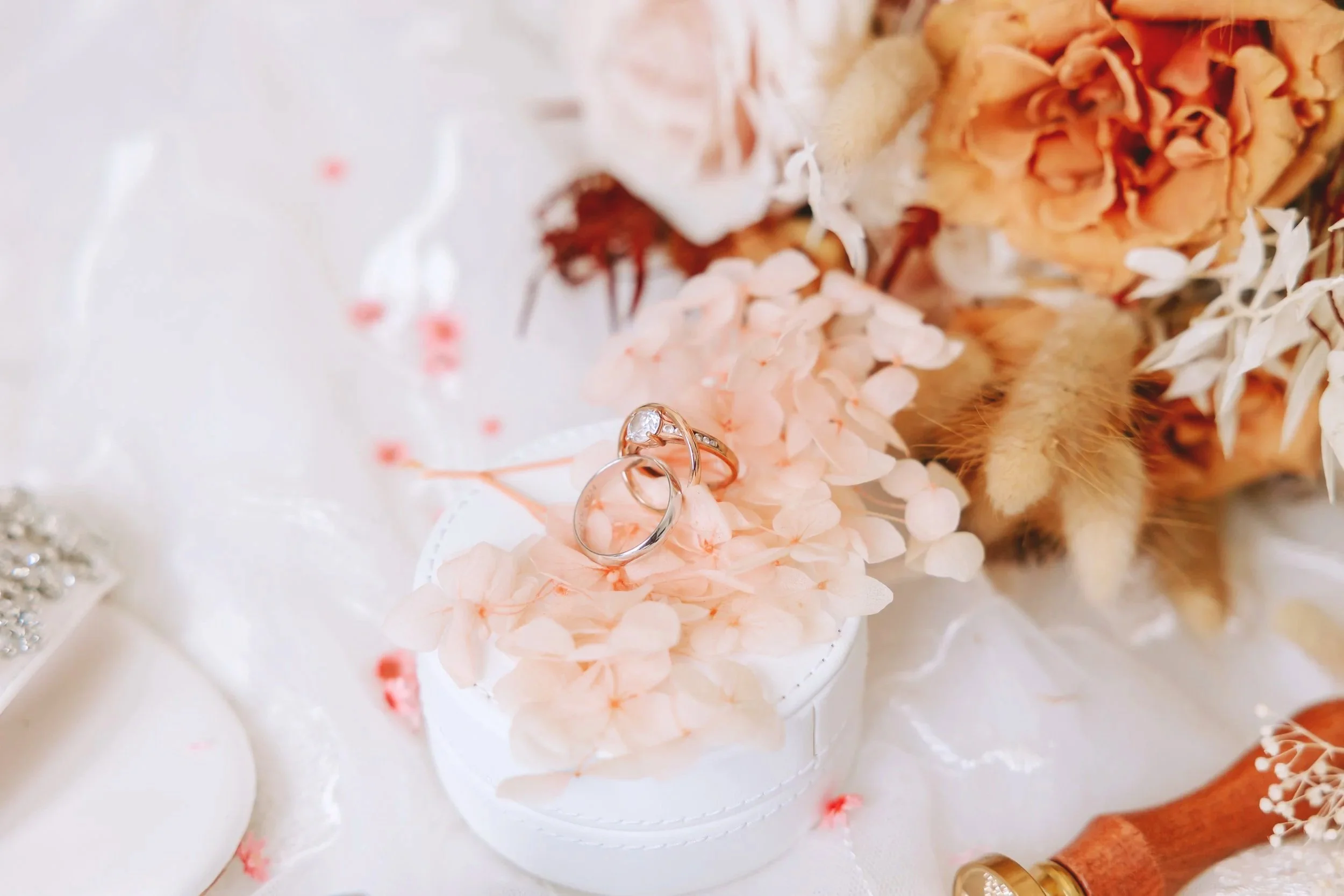 Anneaux de mariage posés sur des fleurs pâles, avec un gâteau en arrière-plan lors d'une célébration