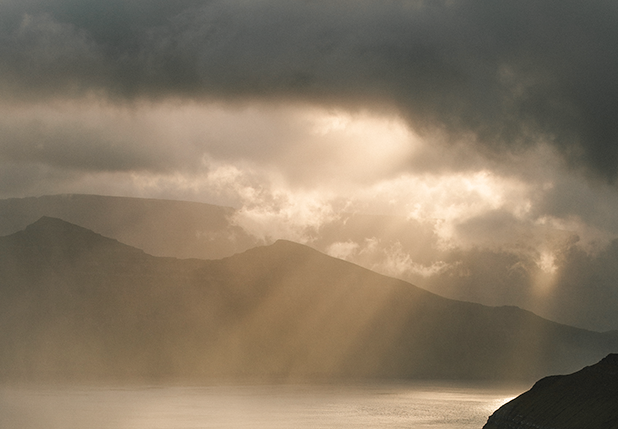 A landscape scene featuring cloudy skies over mountain ranges with a body of water in the foreground.