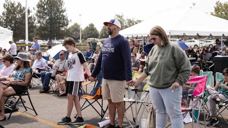 Group of people participating in an outdoor prayer session, standing with their hands joined.