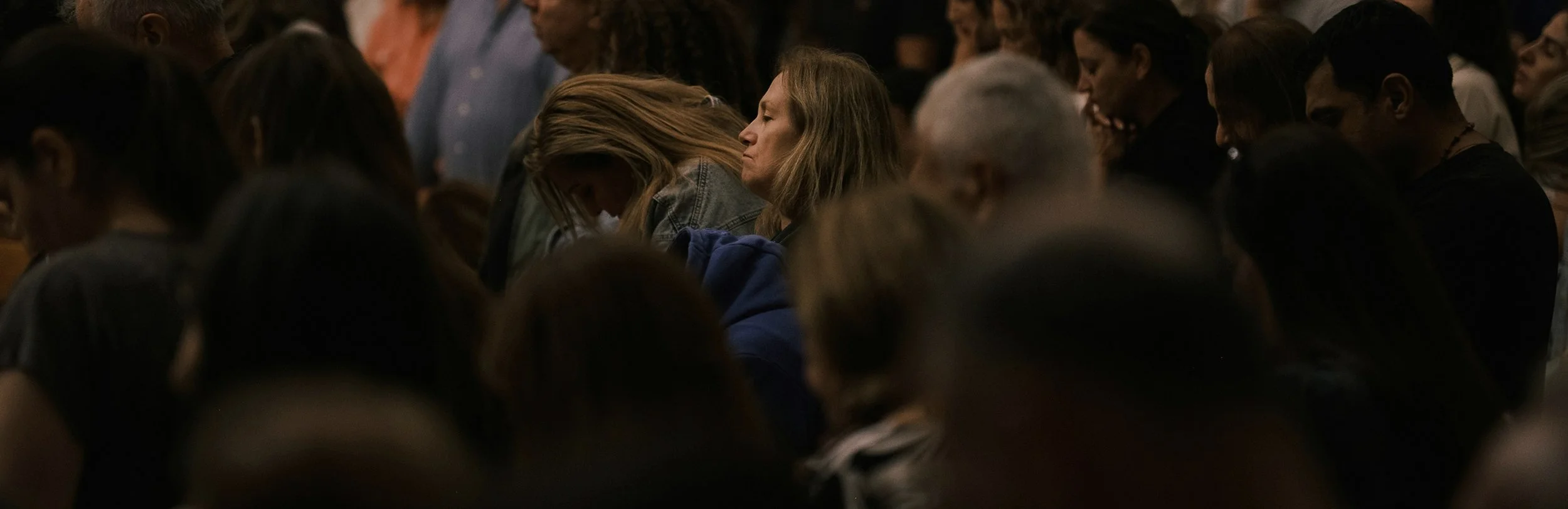 A group of people sitting closely together with their heads bowed, appearing to be in prayer or contemplation.