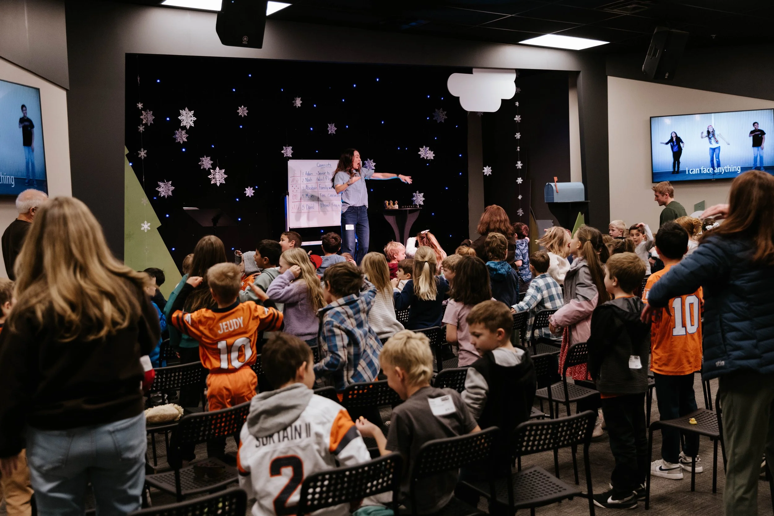Group of young children sitting on the floor, making funny faces at an indoor event.