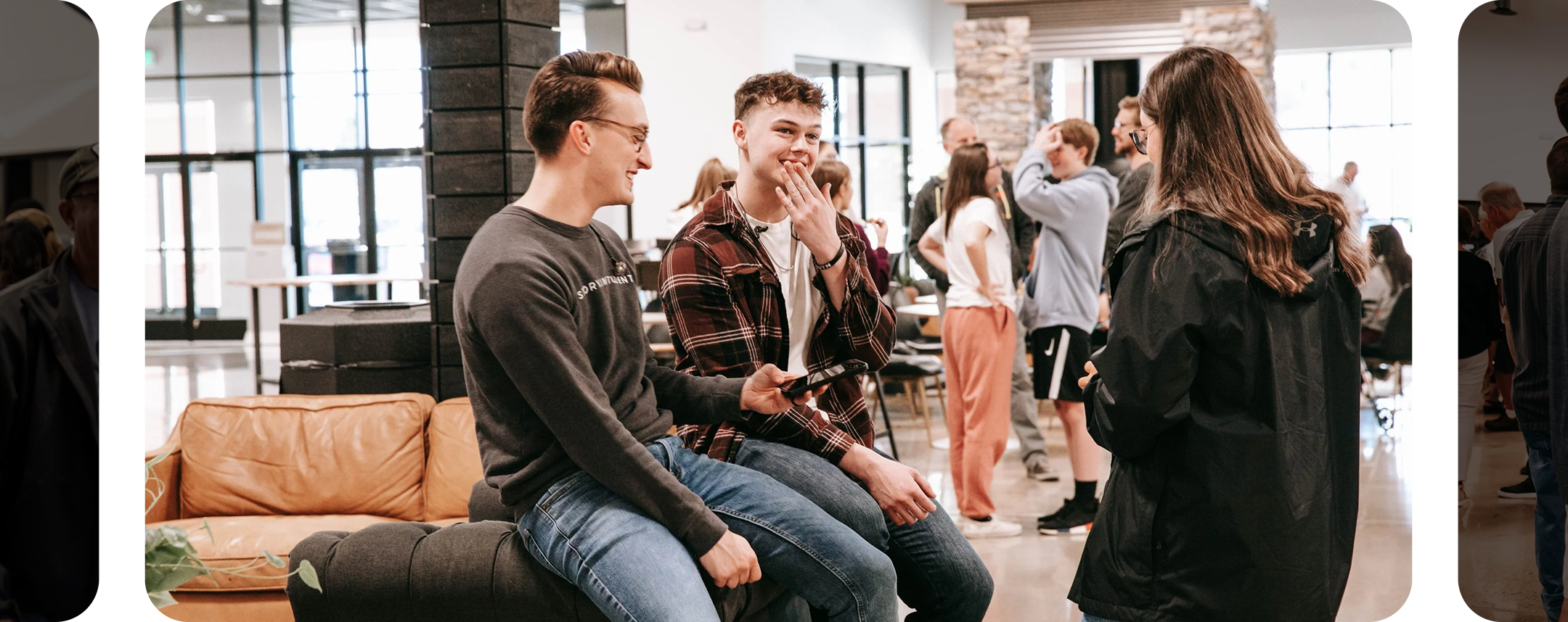 Three young people conversing in a busy indoor space, with other people in the background.