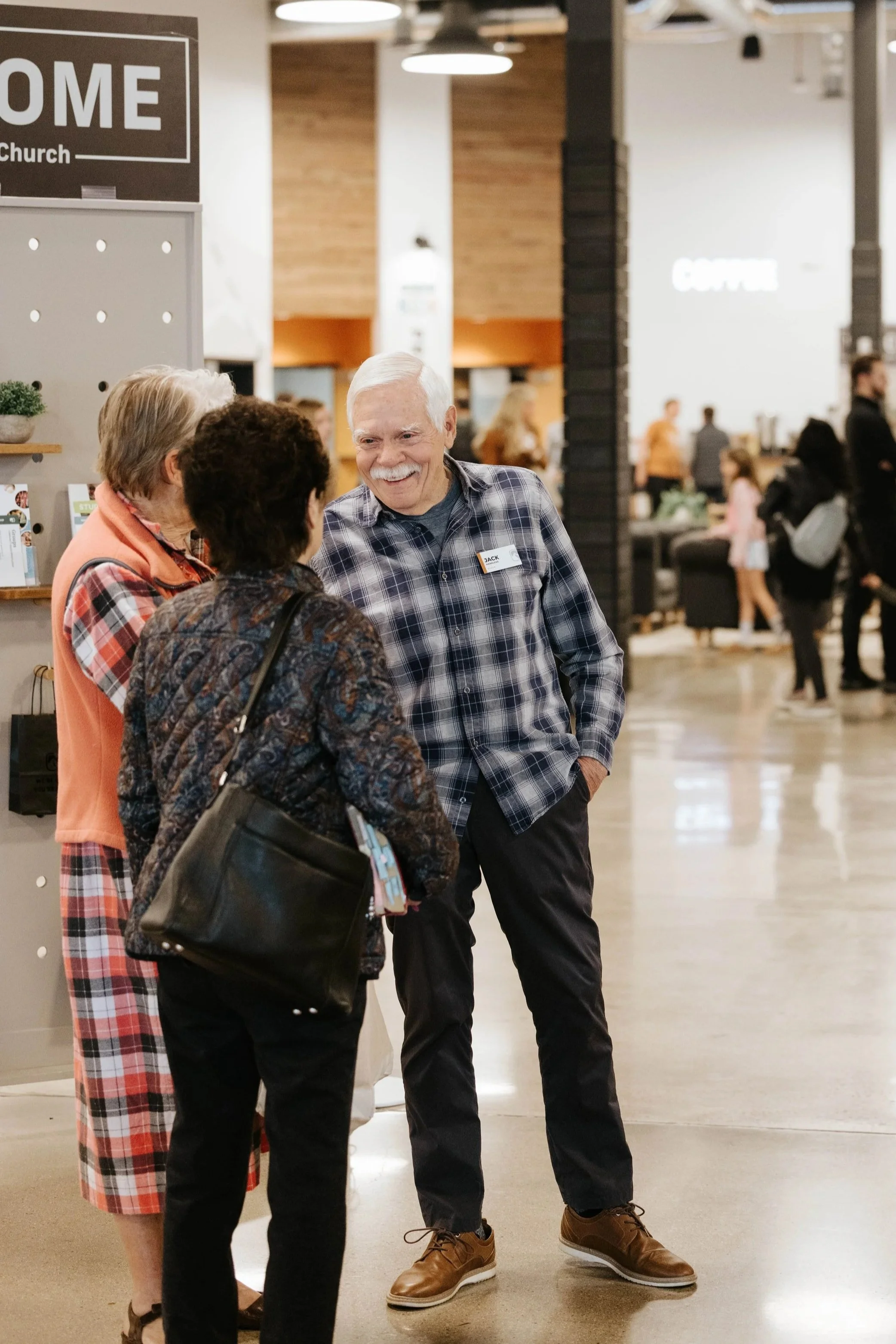 Three elderly people standing and talking in a shopping mall.
