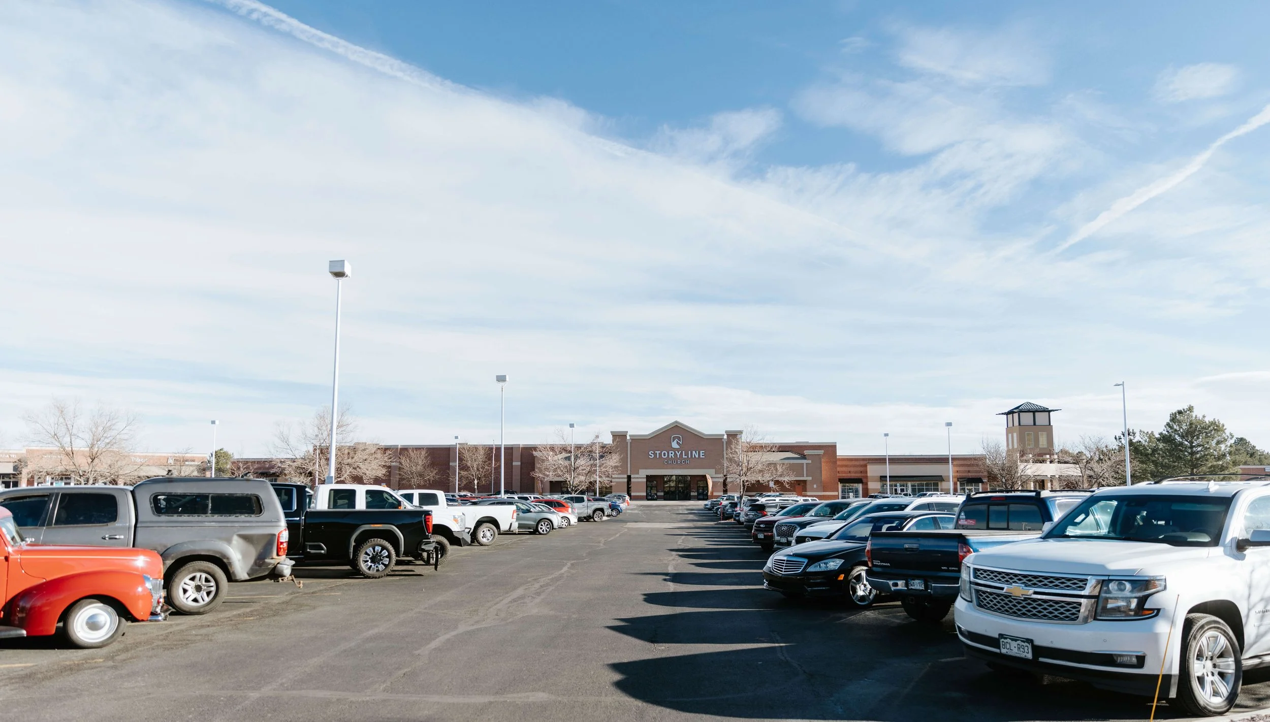 A large parking lot filled with various cars in front of a brick church building named STORYLINE CHURCH under a blue sky with scattered clouds.